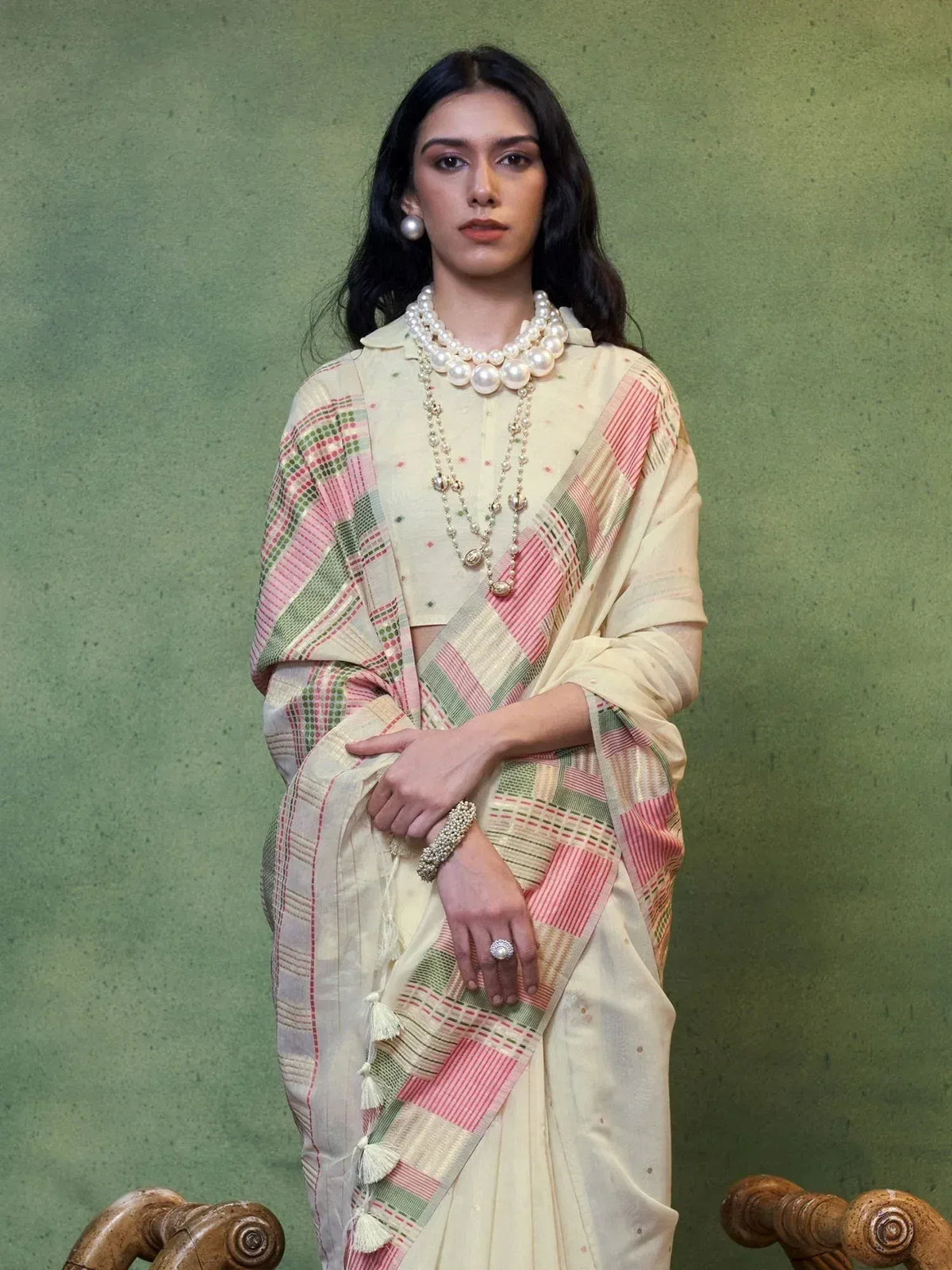 Woman in elegant cream saree with pink green plaid border, styled with pearl jewelry for ethnic wear