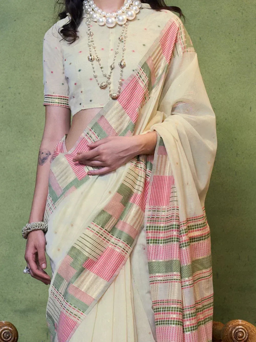 Cream saree with pink green geometric border, paired with dotted blouse and pearl jewelry