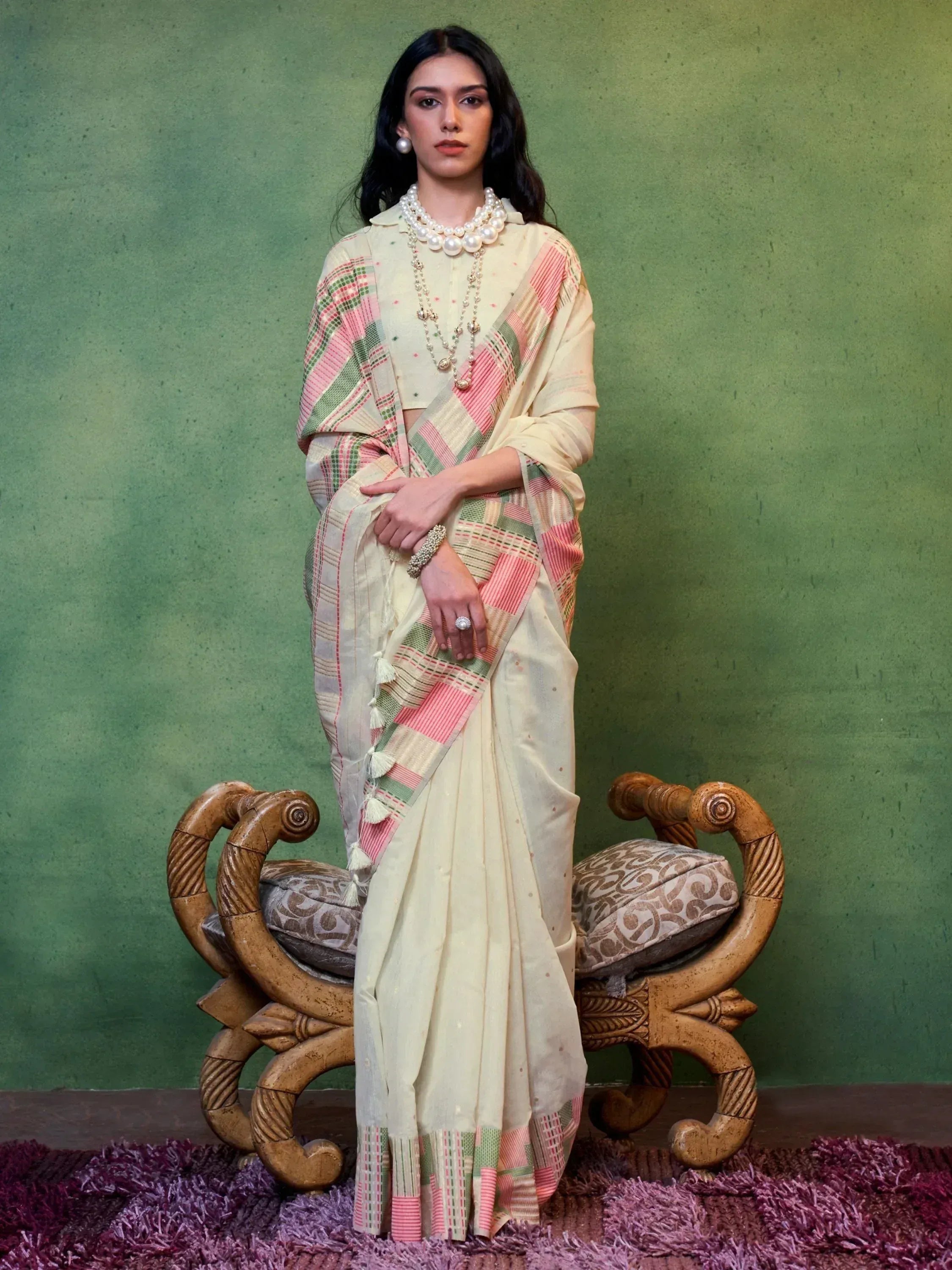 Elegant cream saree with pink green checkered border, paired with pearl jewelry, perfect for ethnic occasions.