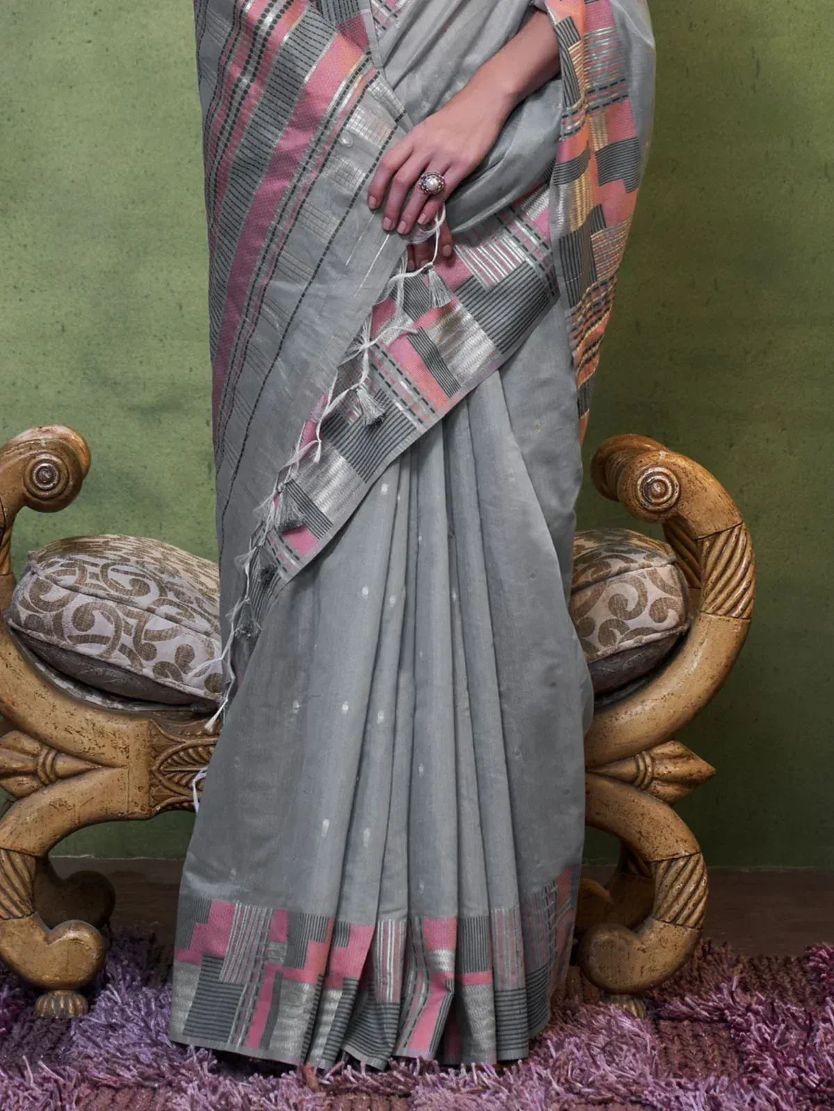 Grey saree with pink and silver geometric border, ethnic Indian wear, styled with tassels and ornate chair