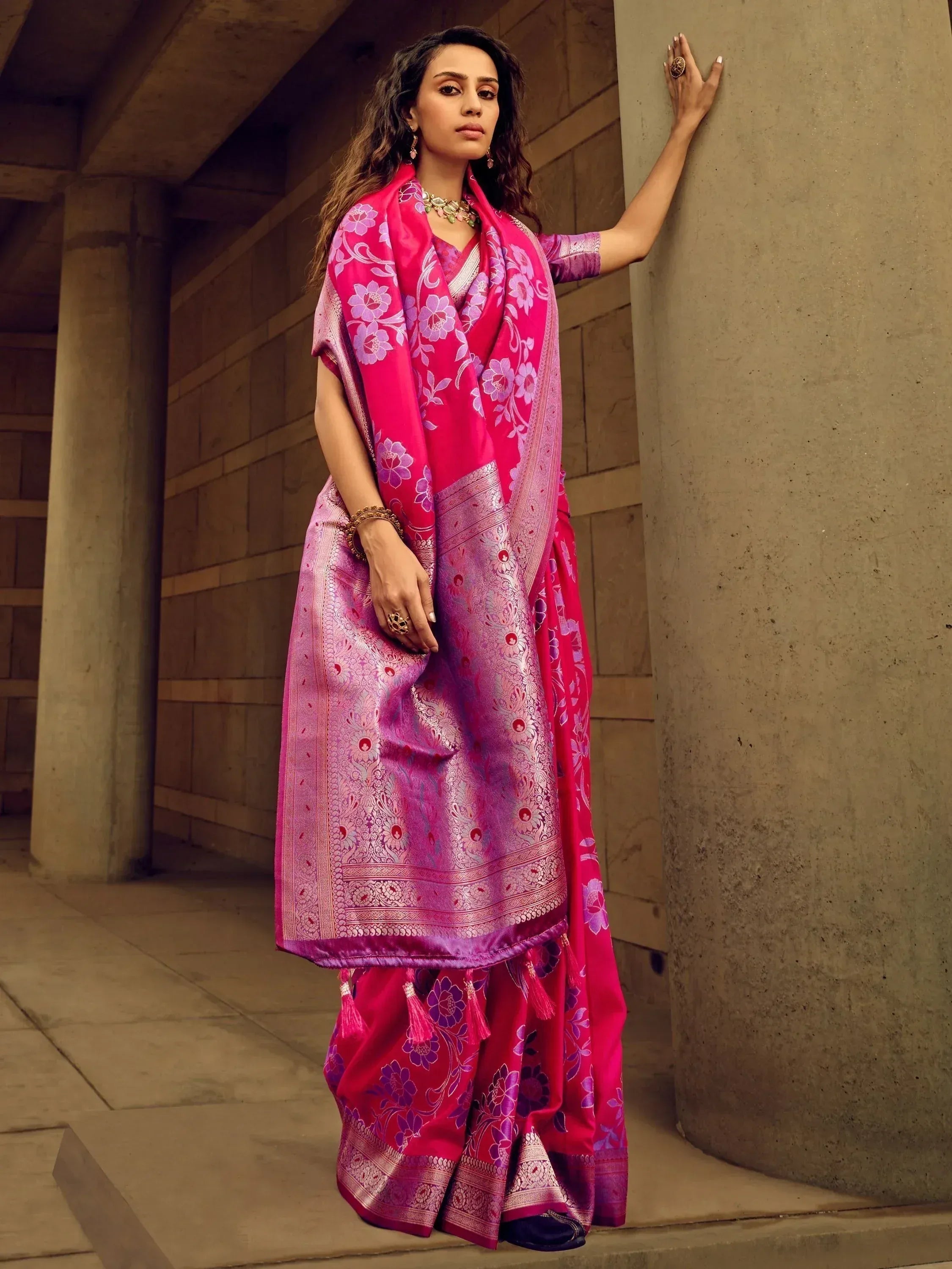 Woman in vibrant pink floral saree with gold border, styled with ethnic jewelry, perfect for Indian occasions.