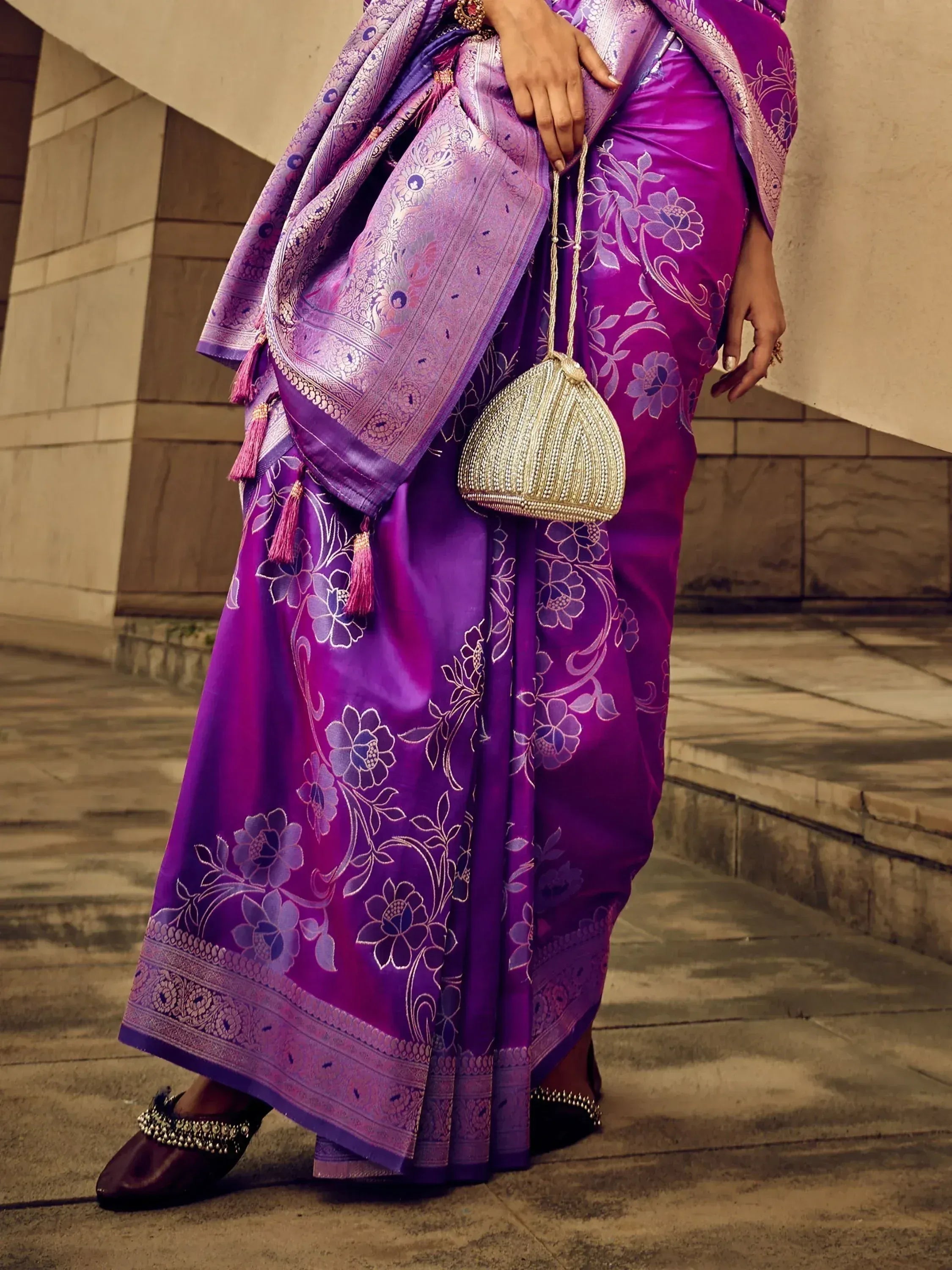 Purple floral saree with gold embroidery, tassels, and matching potli bag for Indian ethnic wear