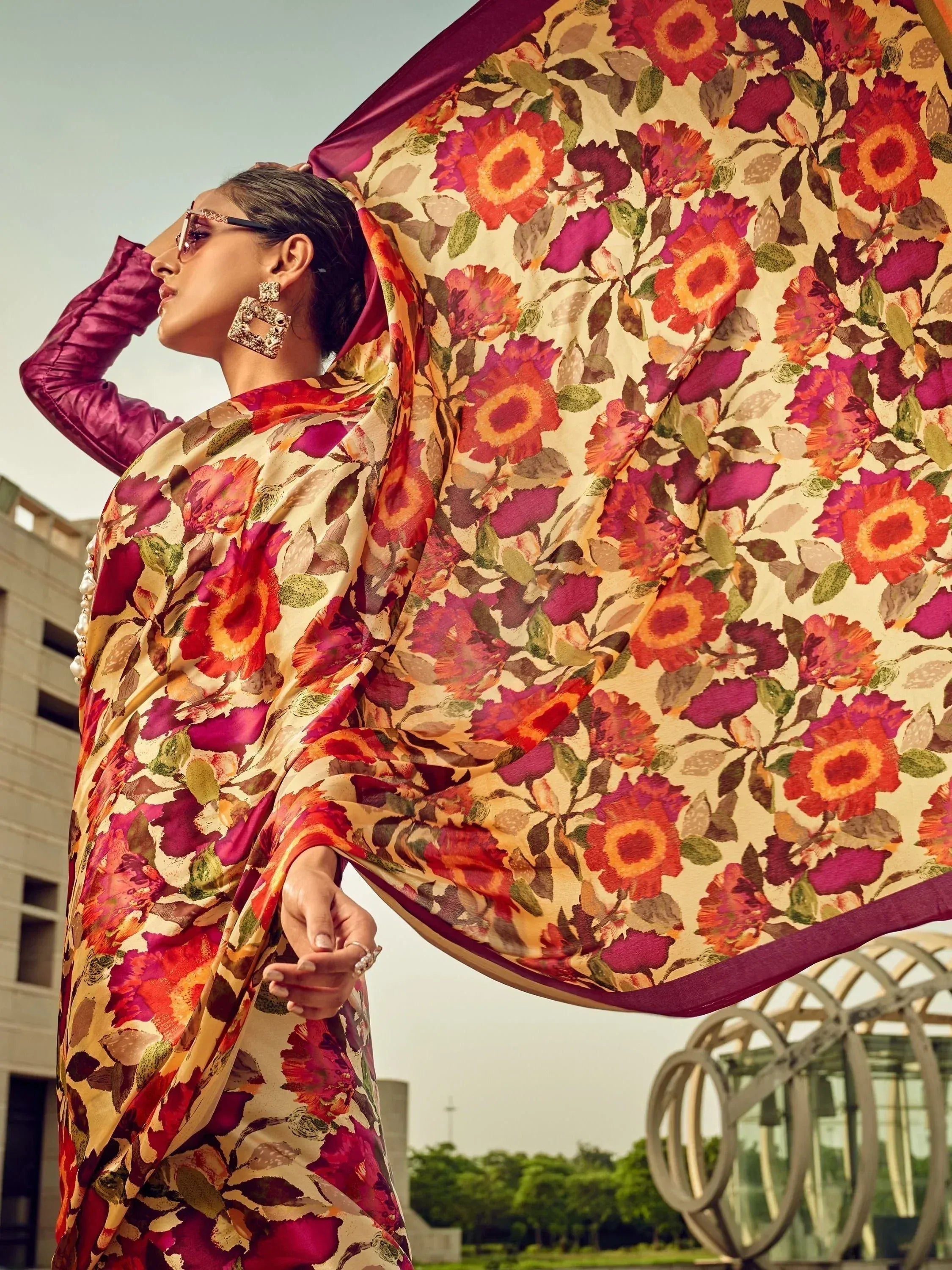 Woman in vibrant floral saree with purple blouse, stylish sunglasses, and statement earrings, showcasing ethnic Indian wear.