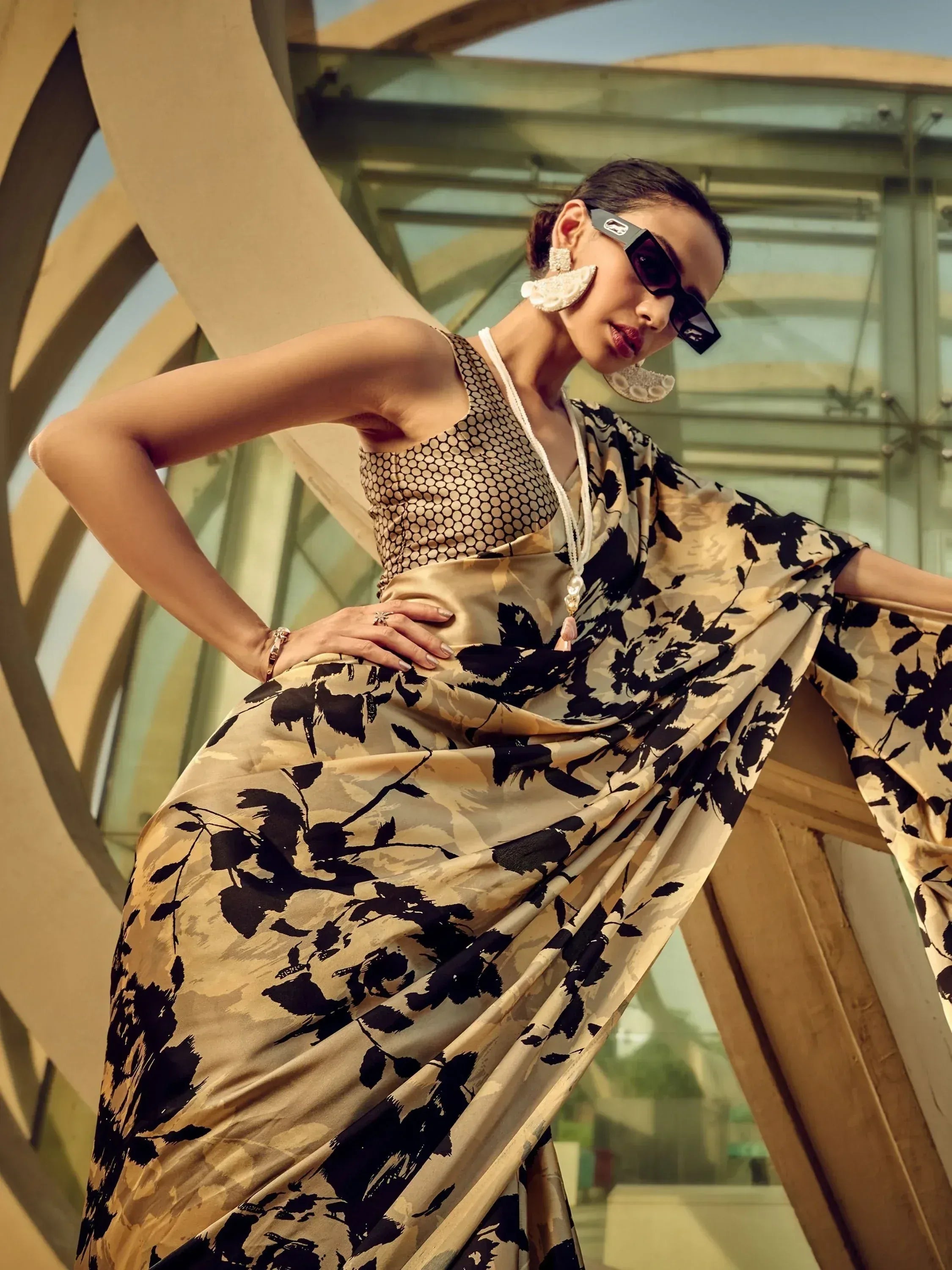 Stylish woman in black and beige floral saree with polka dot blouse, modern sunglasses, and statement earrings.