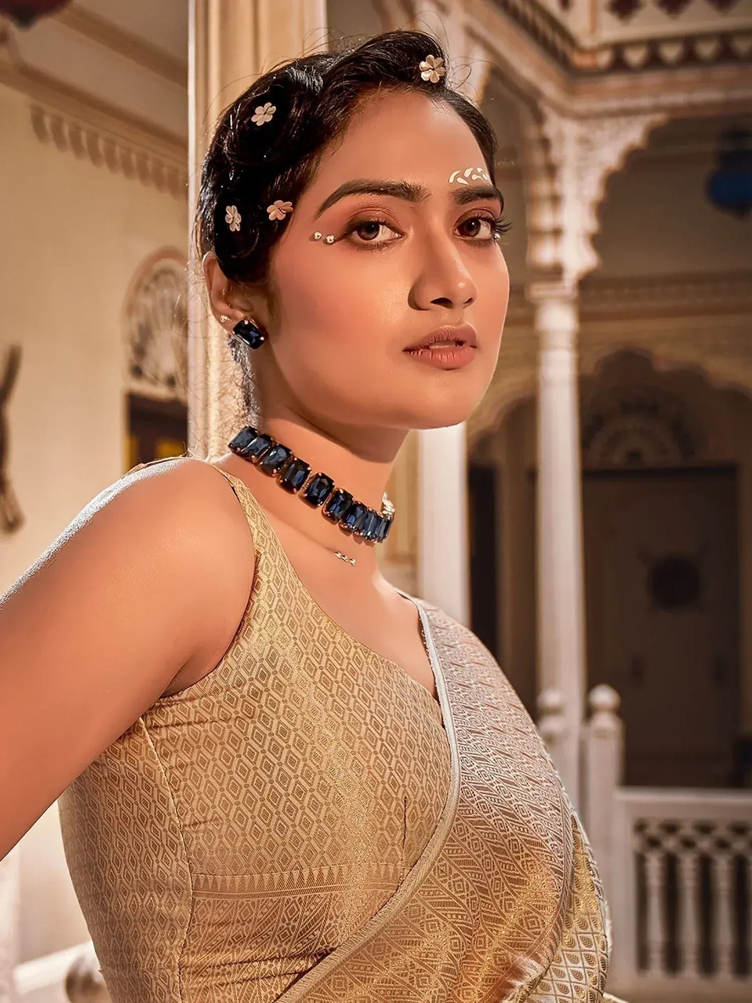 Woman in elegant gold ethnic gown with floral hair accessories and blue gem choker, traditional Indian wear