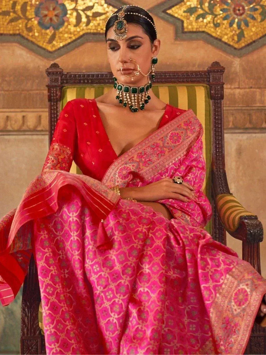 Woman in vibrant pink and red designer saree with intricate embroidery, traditional jewelry, seated on ornate chair