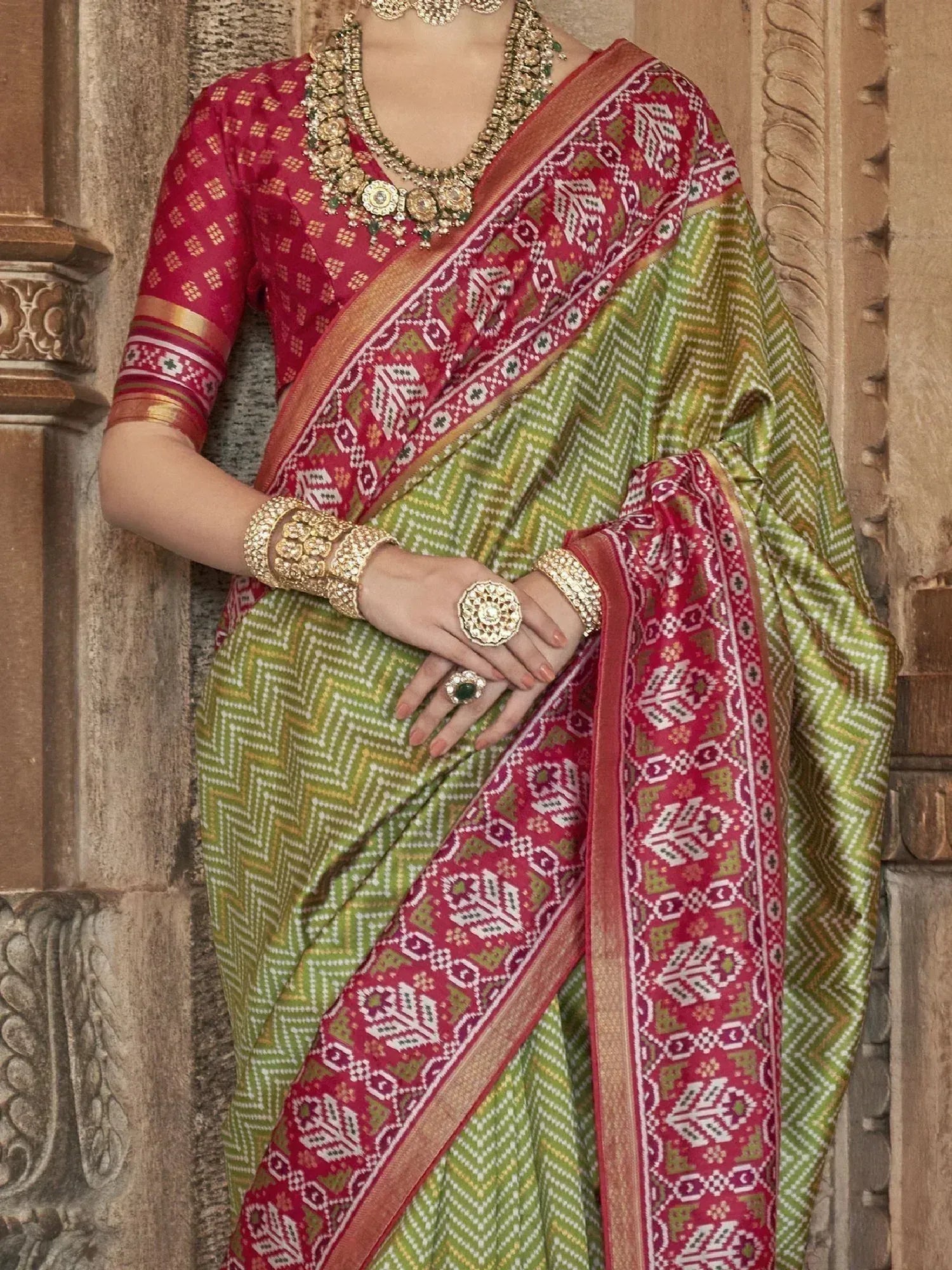 Green and red ethnic saree with geometric print, paired with gold jewelry and blouse, perfect for Indian occasions.