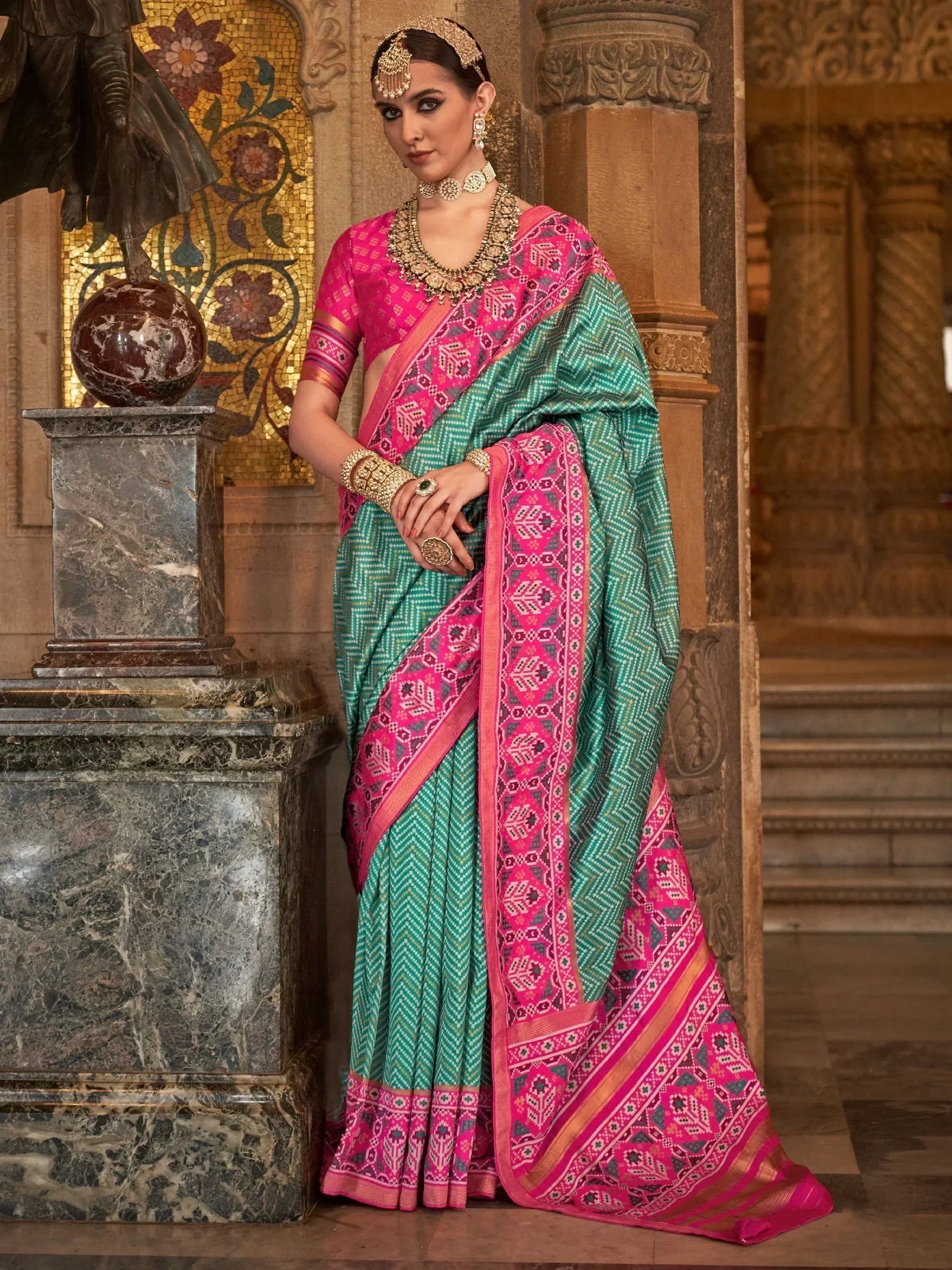 Woman in vibrant green and pink ethnic saree with intricate patterns, traditional jewelry, and temple backdrop