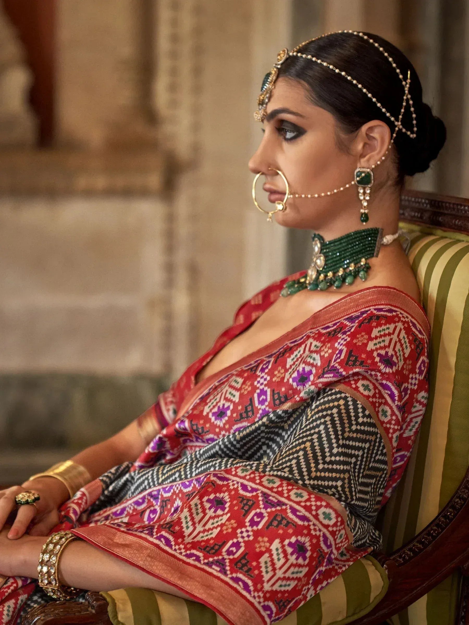 Woman in red and black patterned saree with green jewelry, traditional Indian ethnic wear