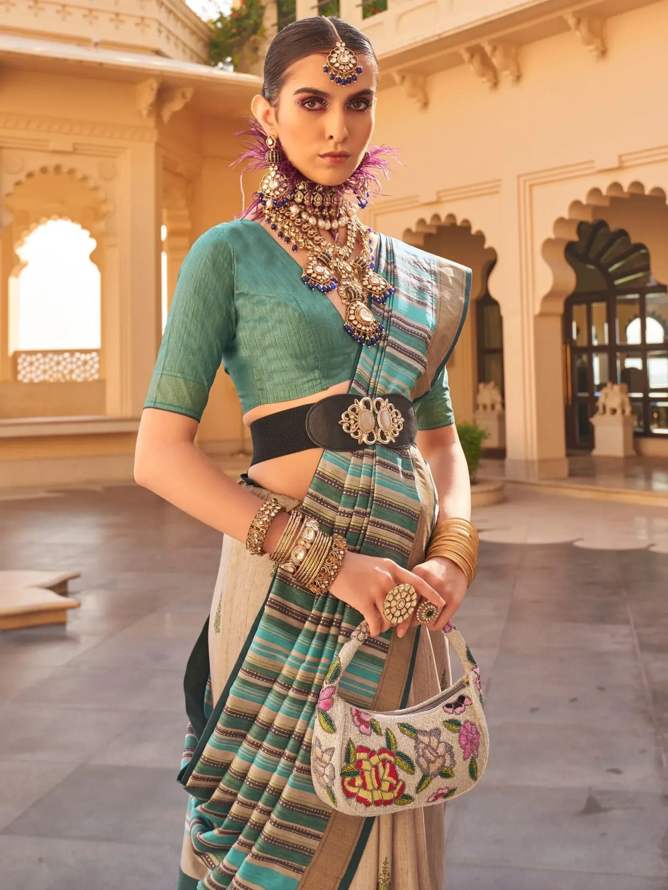Woman in teal striped saree with gold jewelry and floral handbag, Indian ethnic wear