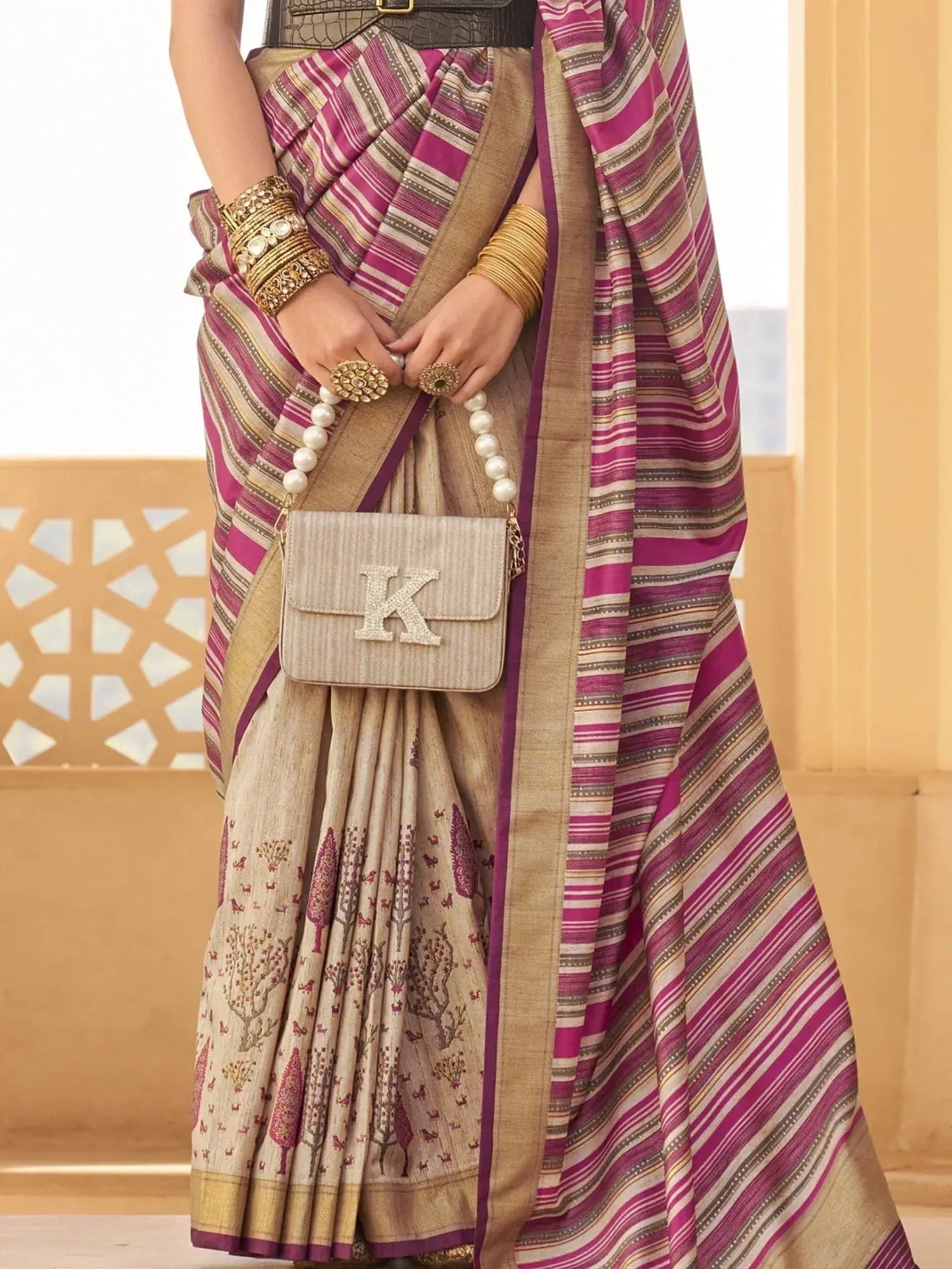 Woman in ethnic saree with purple stripes and tree print, paired with gold jewelry and pearl bag