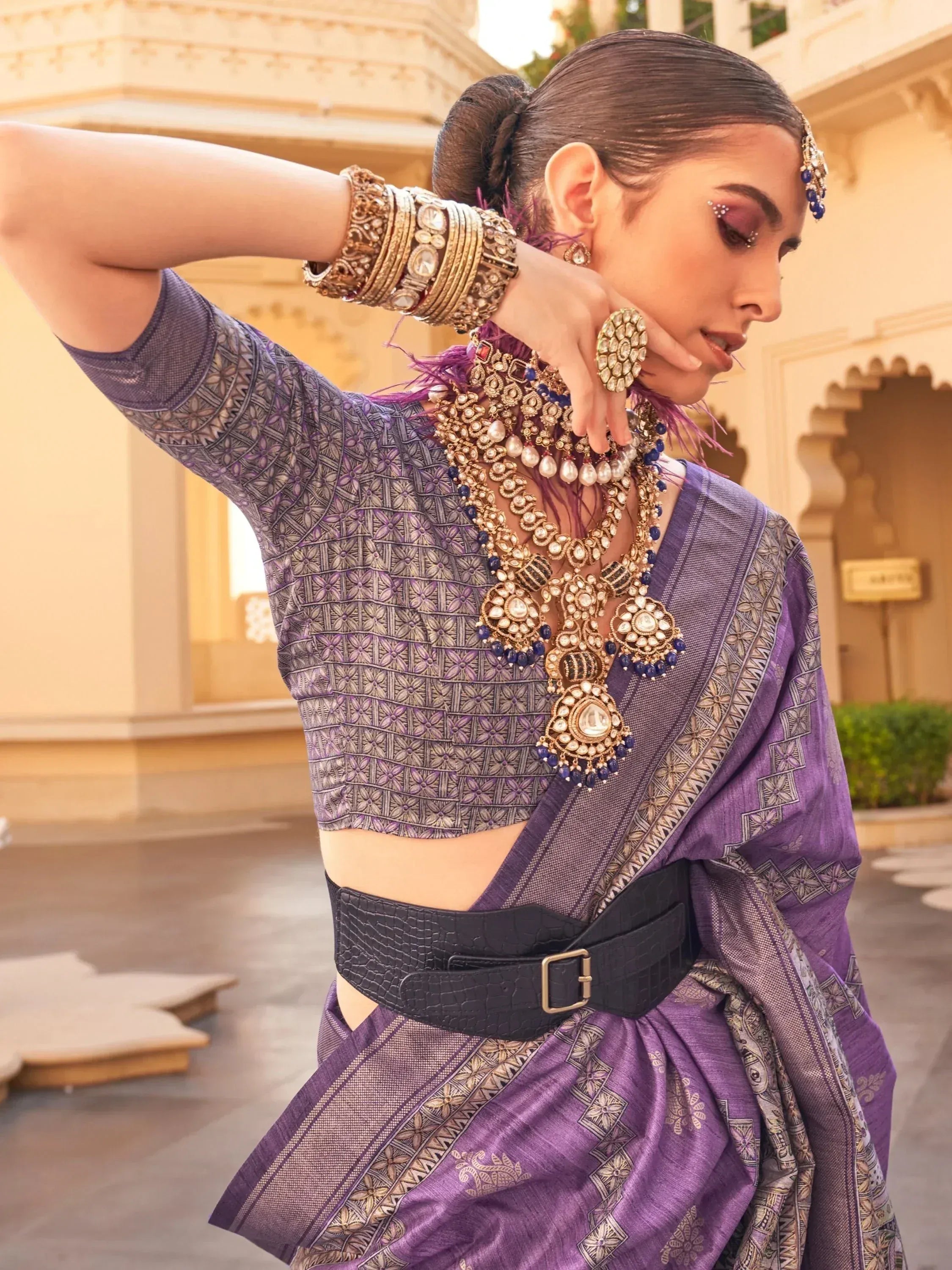Purple printed saree with designer blouse, statement jewelry, and black belt for ethnic wear
