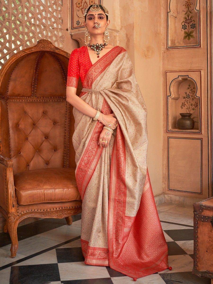 Elegant beige and red designer saree with intricate border, paired with matching blouse and traditional jewelry
