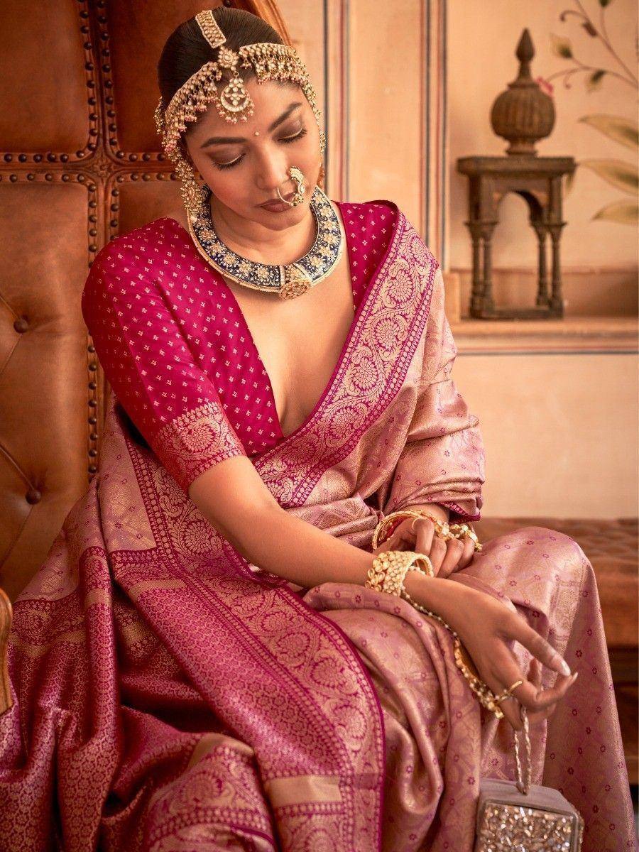 Elegant Indian woman in pink designer saree with gold embroidery, traditional jewelry, and maang tikka, seated on leather chair.