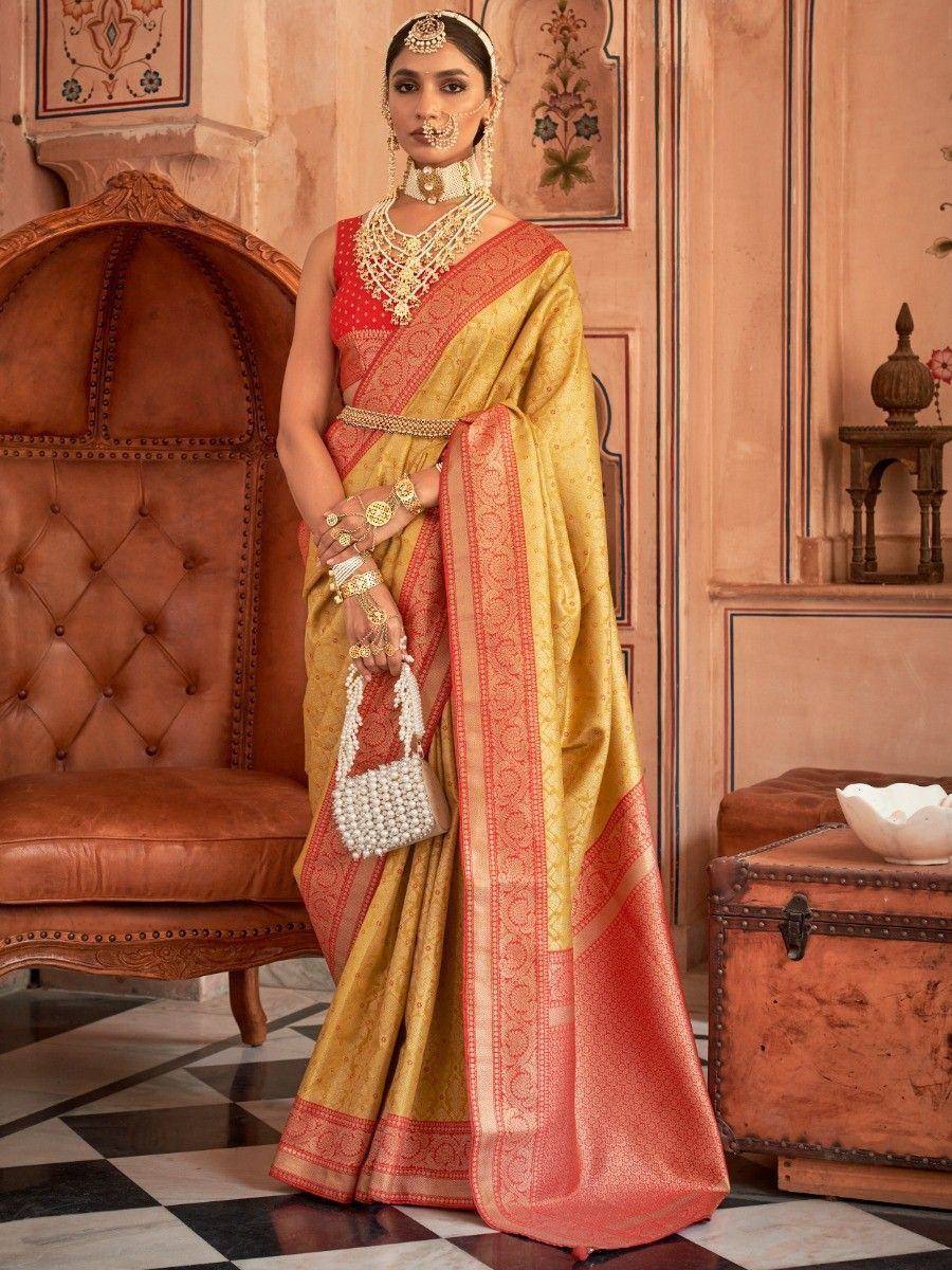 Golden and red designer saree with intricate embroidery, paired with traditional jewelry and a pearl clutch.