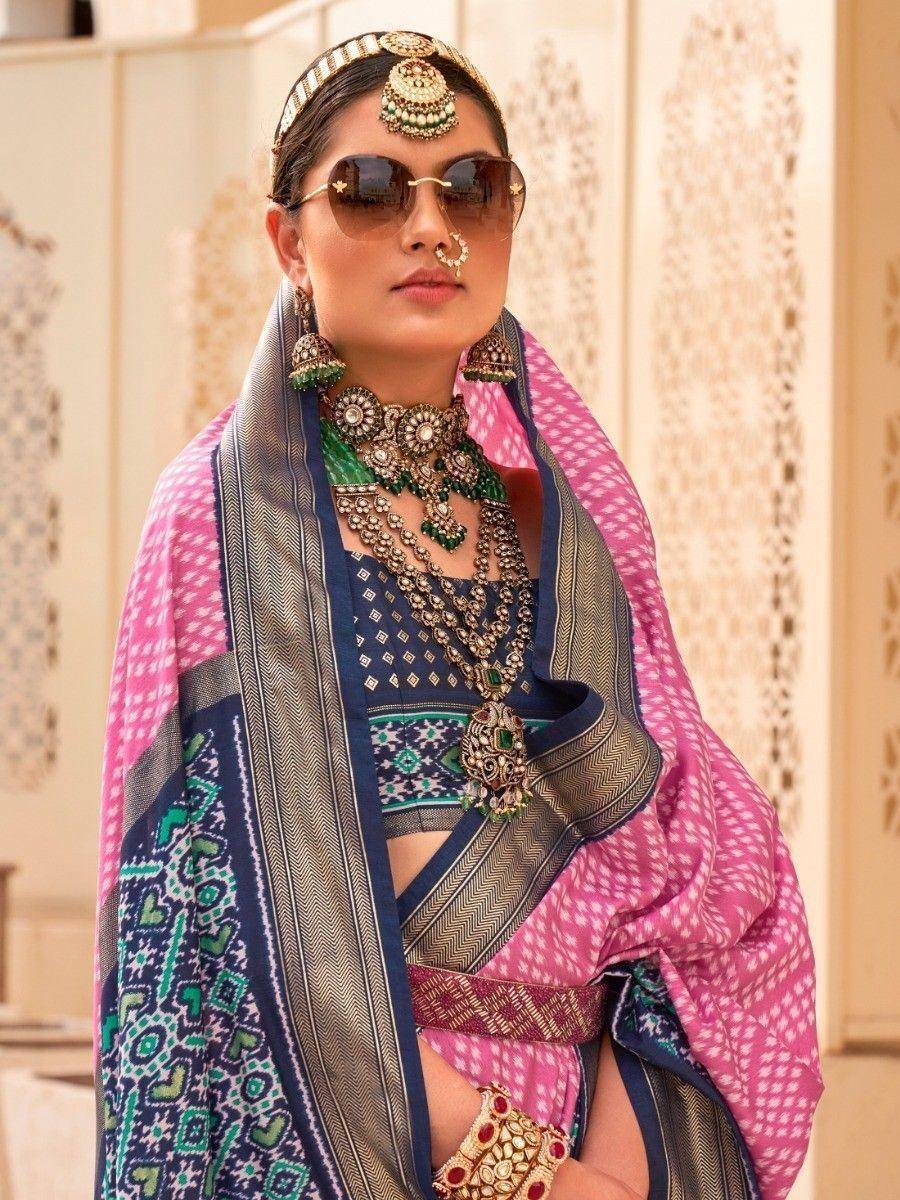 Woman in vibrant pink and blue ethnic saree with intricate jewelry and sunglasses, showcasing traditional Indian fashion.