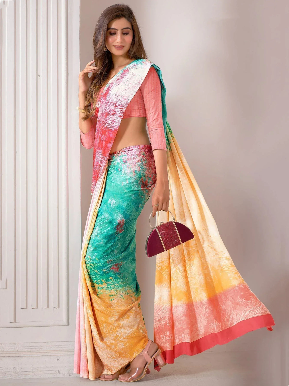 Woman in vibrant printed saree with pink blouse, floral ombre design, holding clutch, ethnic wear