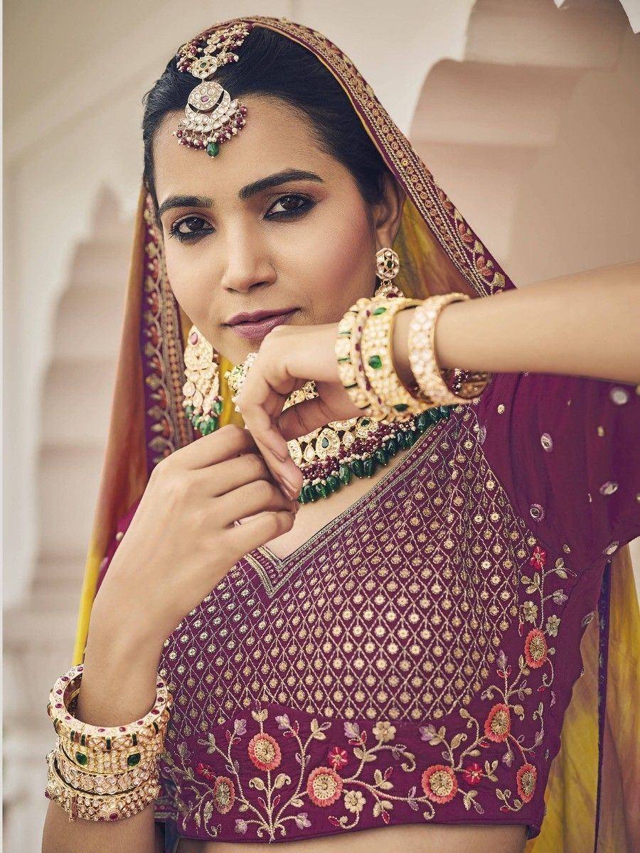 Elegant Indian bride in purple embroidered lehenga choli with gold jewelry and floral detailing