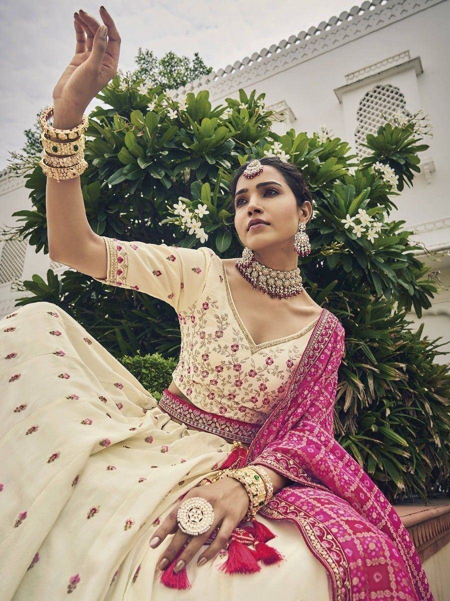 Elegant cream and pink embroidered lehenga choli with traditional jewelry, perfect for Indian weddings and festivals.