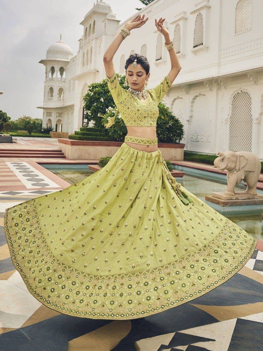 Woman twirling in elegant light green lehenga choli with mirror work, set against palace backdrop