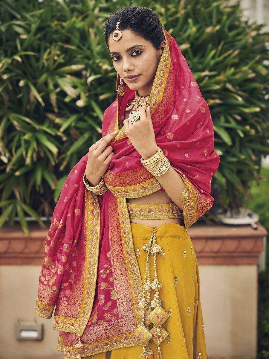 Woman in yellow lehenga choli with pink dupatta, gold embroidery, and traditional Indian jewelry
