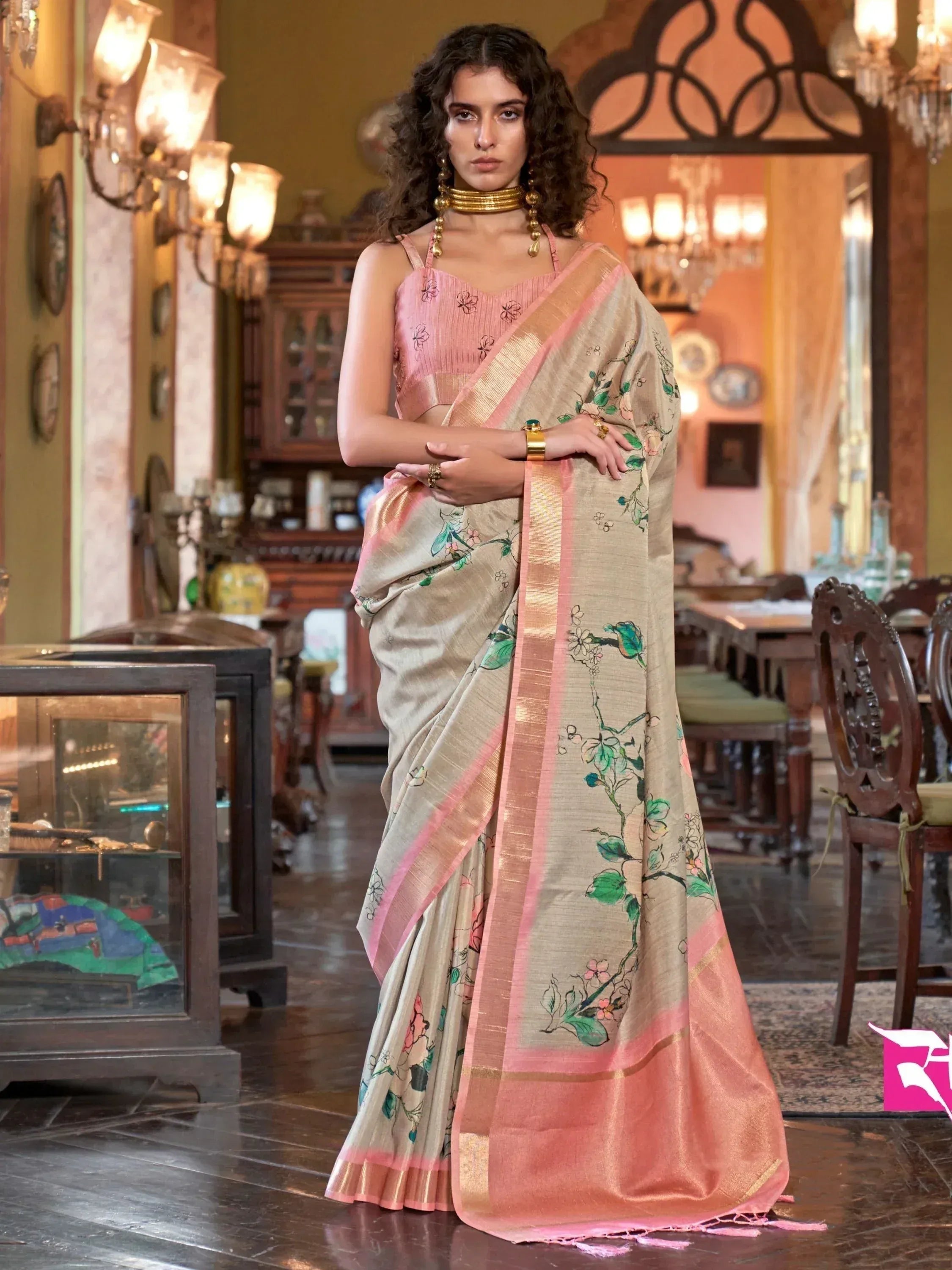 Woman in elegant beige saree with floral print and pink border, paired with matching blouse, ideal for ethnic occasions.