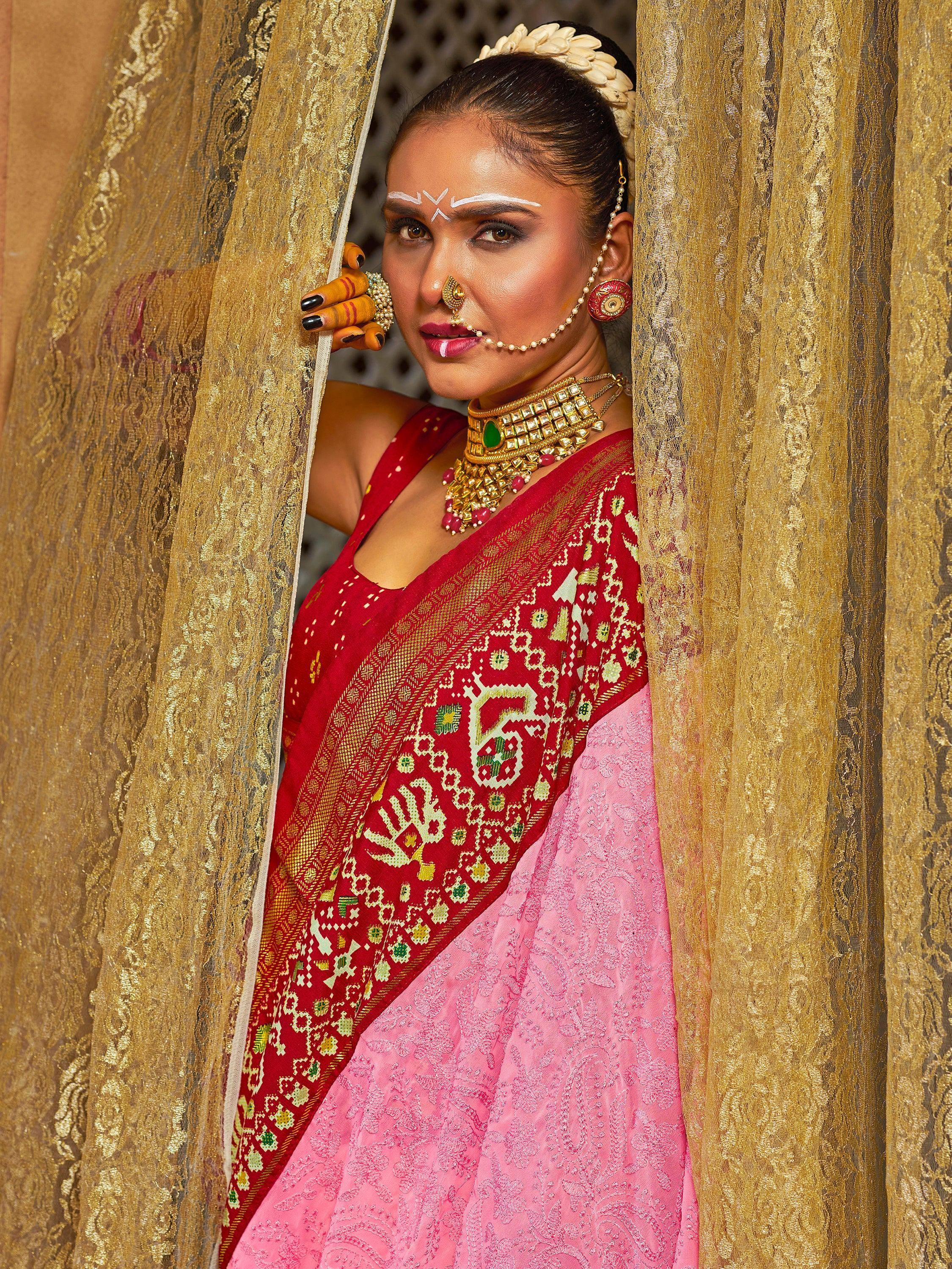 Woman in red and pink ethnic saree with gold jewelry peeking through golden curtains