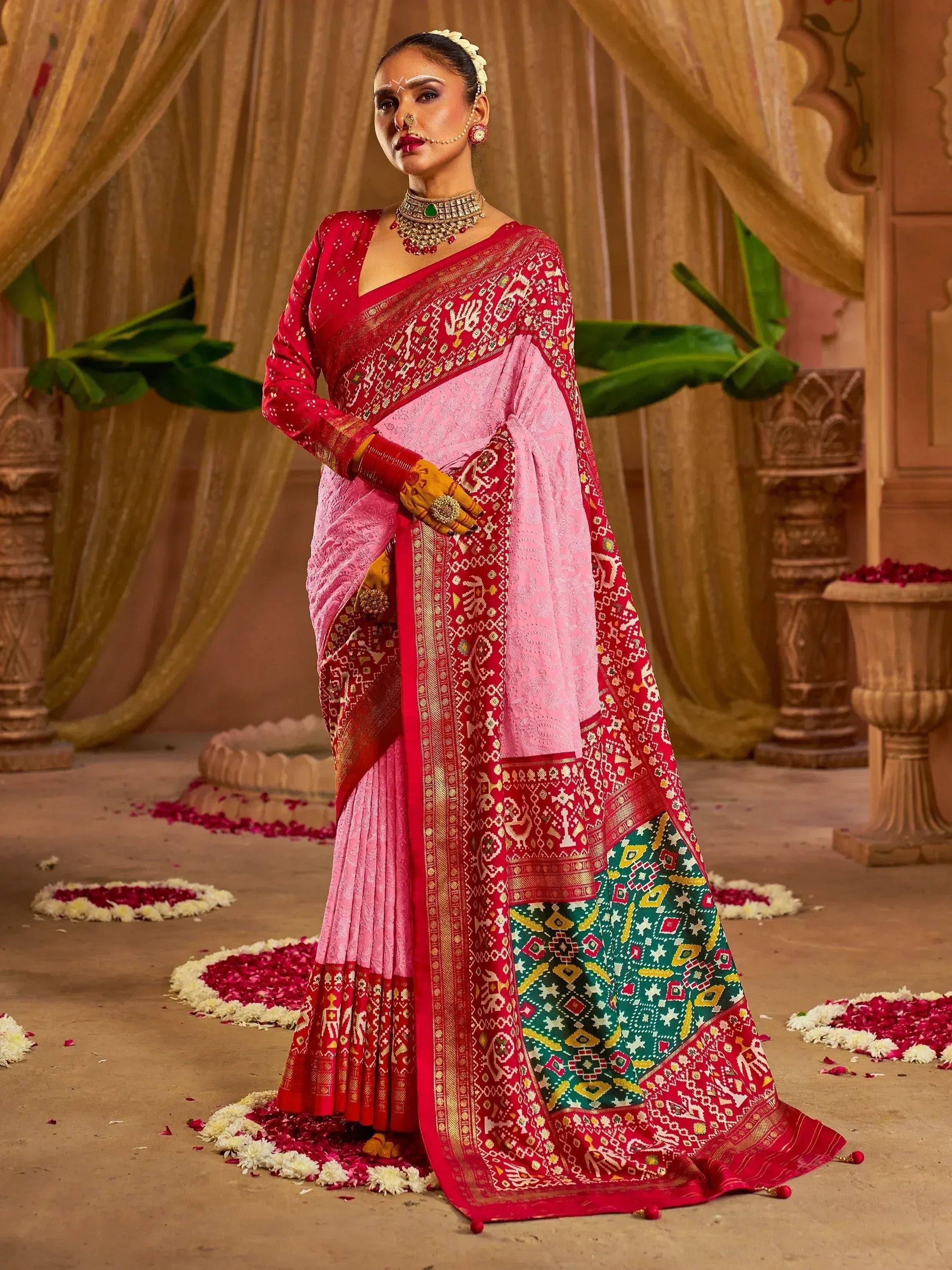 Woman in red and pink ethnic saree with intricate patterns, traditional jewelry, and floral decor
