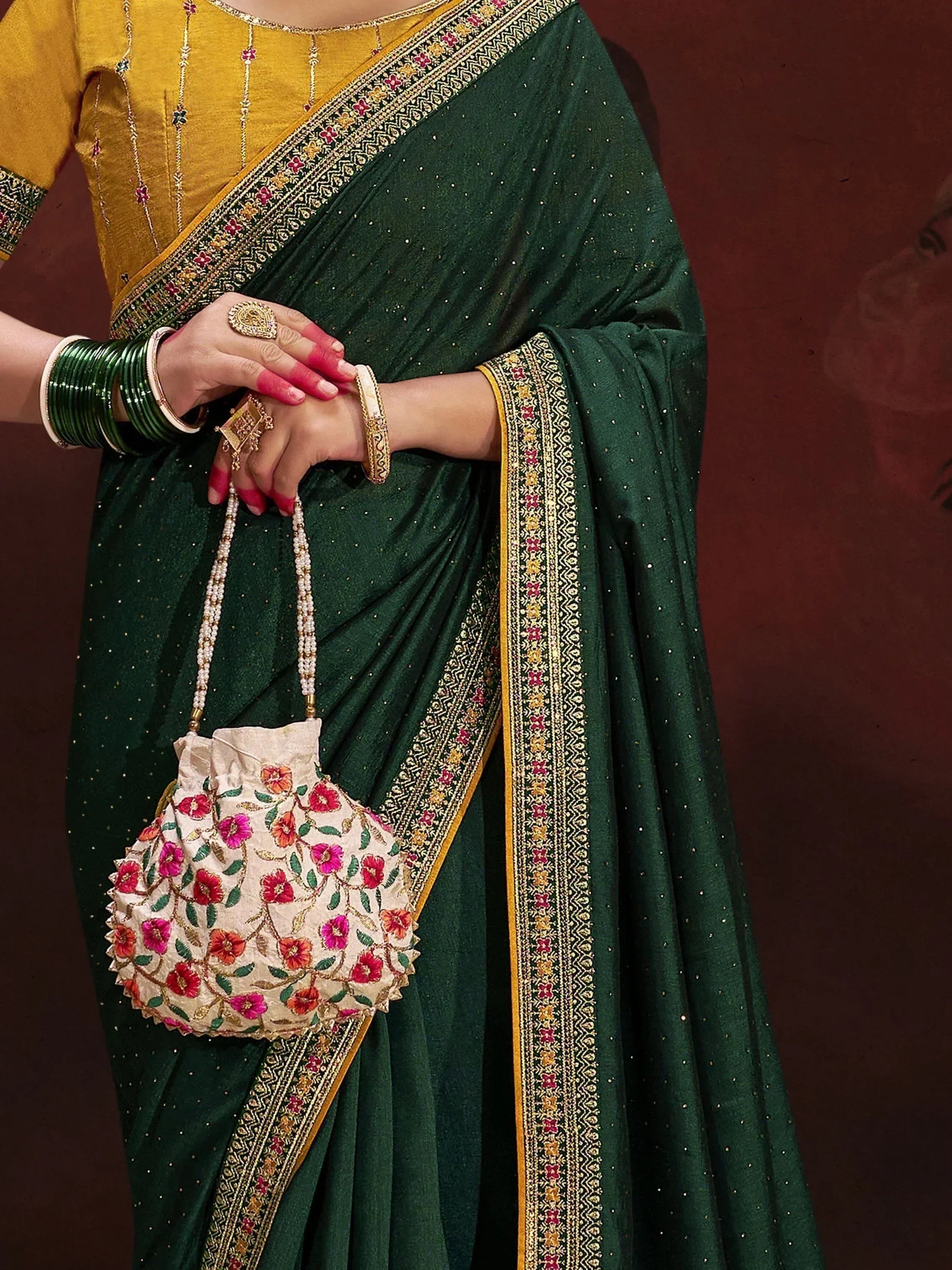 Emerald green saree with gold border, yellow blouse, floral potli bag, and traditional bangles