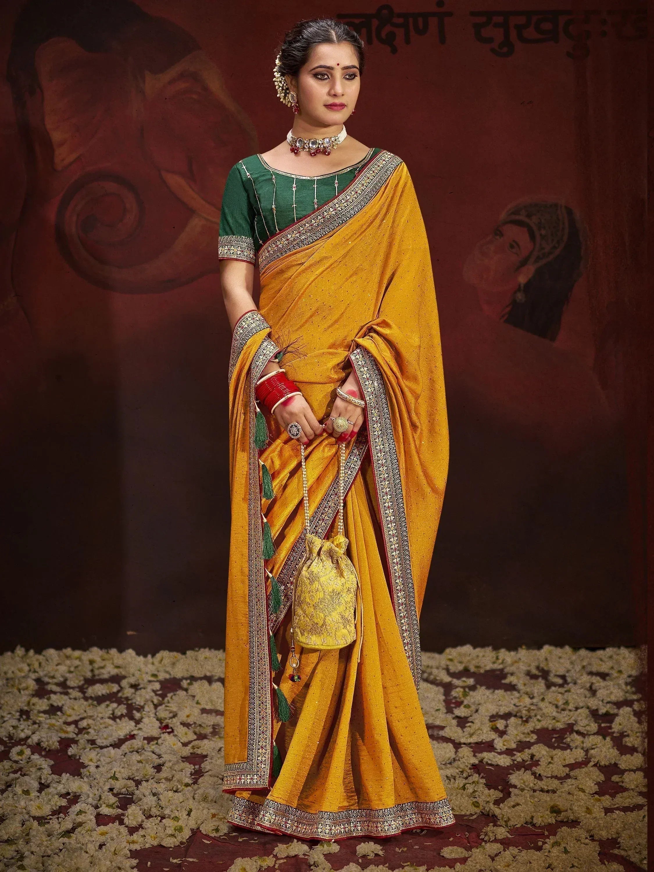 Woman in mustard yellow saree with green blouse, ethnic jewelry, and floral backdrop