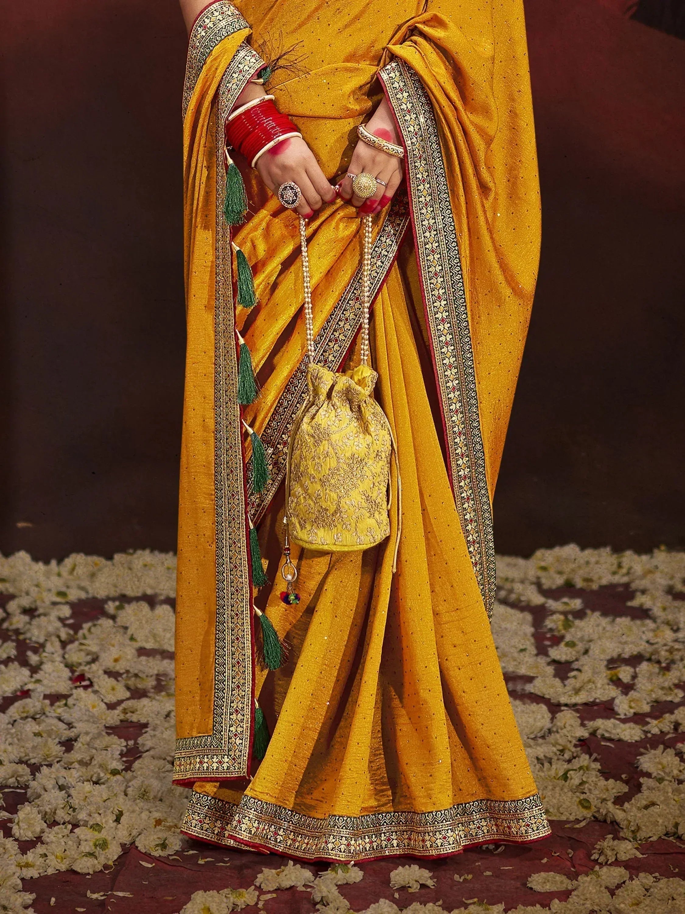Yellow designer saree with gold embroidery, red bangles, and matching potli bag for Indian ethnic wear