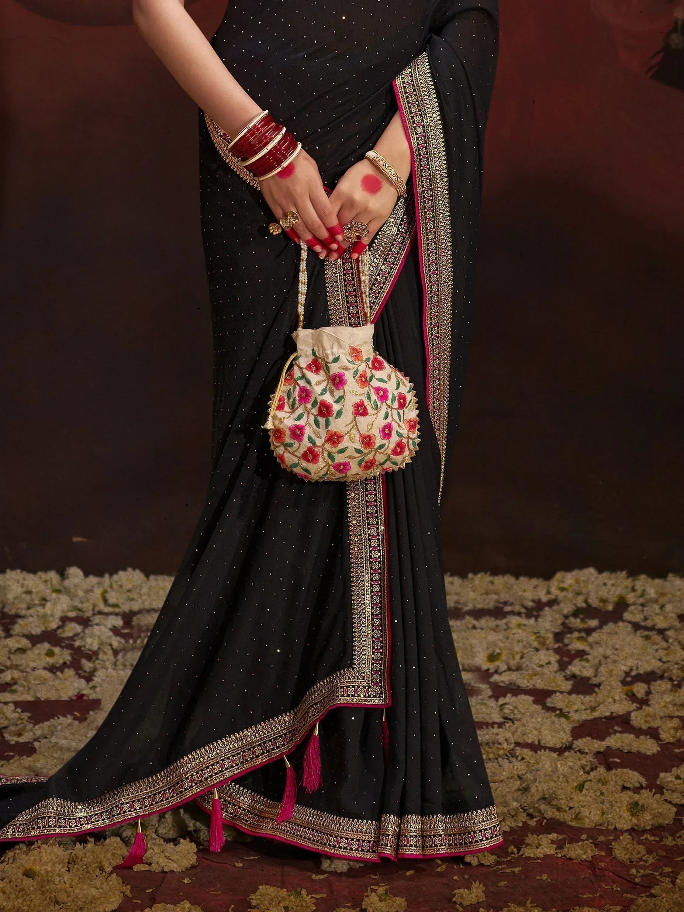Black ethnic saree with gold embroidery, pink tassels, and floral potli bag for Indian weddings