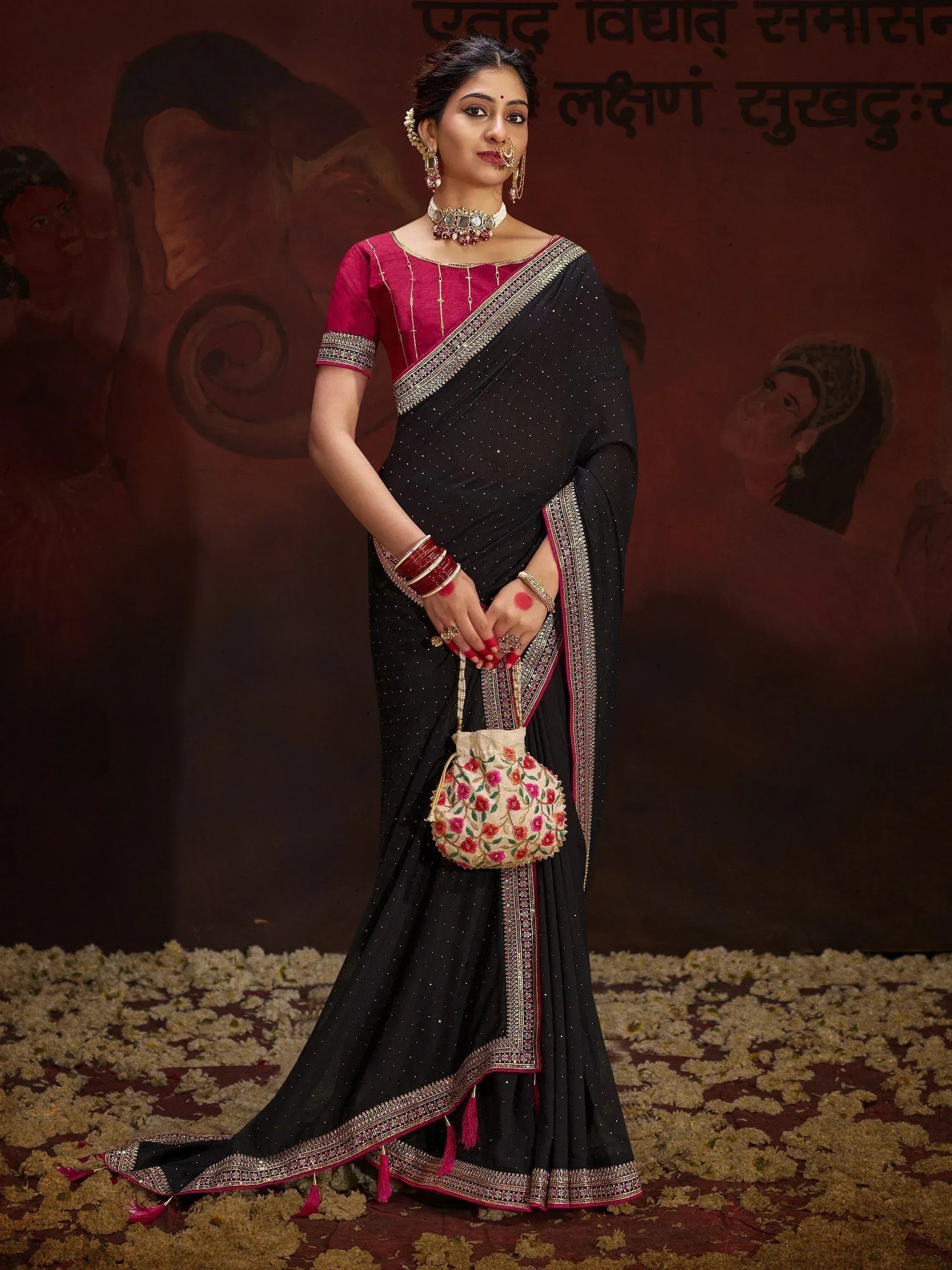 Black and pink ethnic saree with gold border, designer blouse, and floral potli bag for Indian occasions