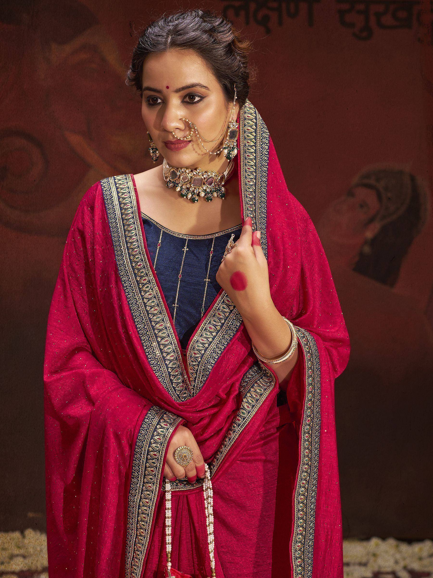 Woman in vibrant pink and navy blue ethnic saree with intricate gold border, traditional jewelry, and bindi