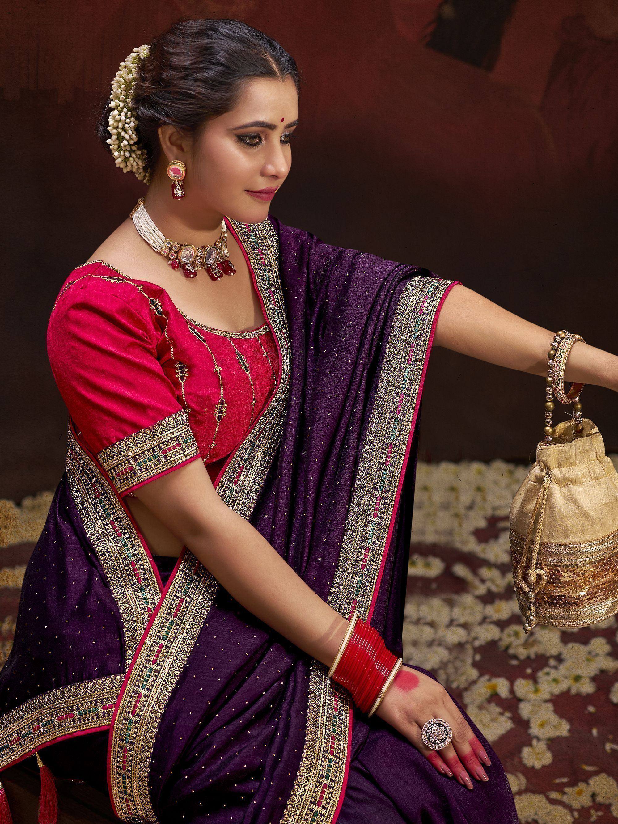 Woman in purple and pink ethnic saree with gold embroidery, traditional jewelry, and floral hair accessory