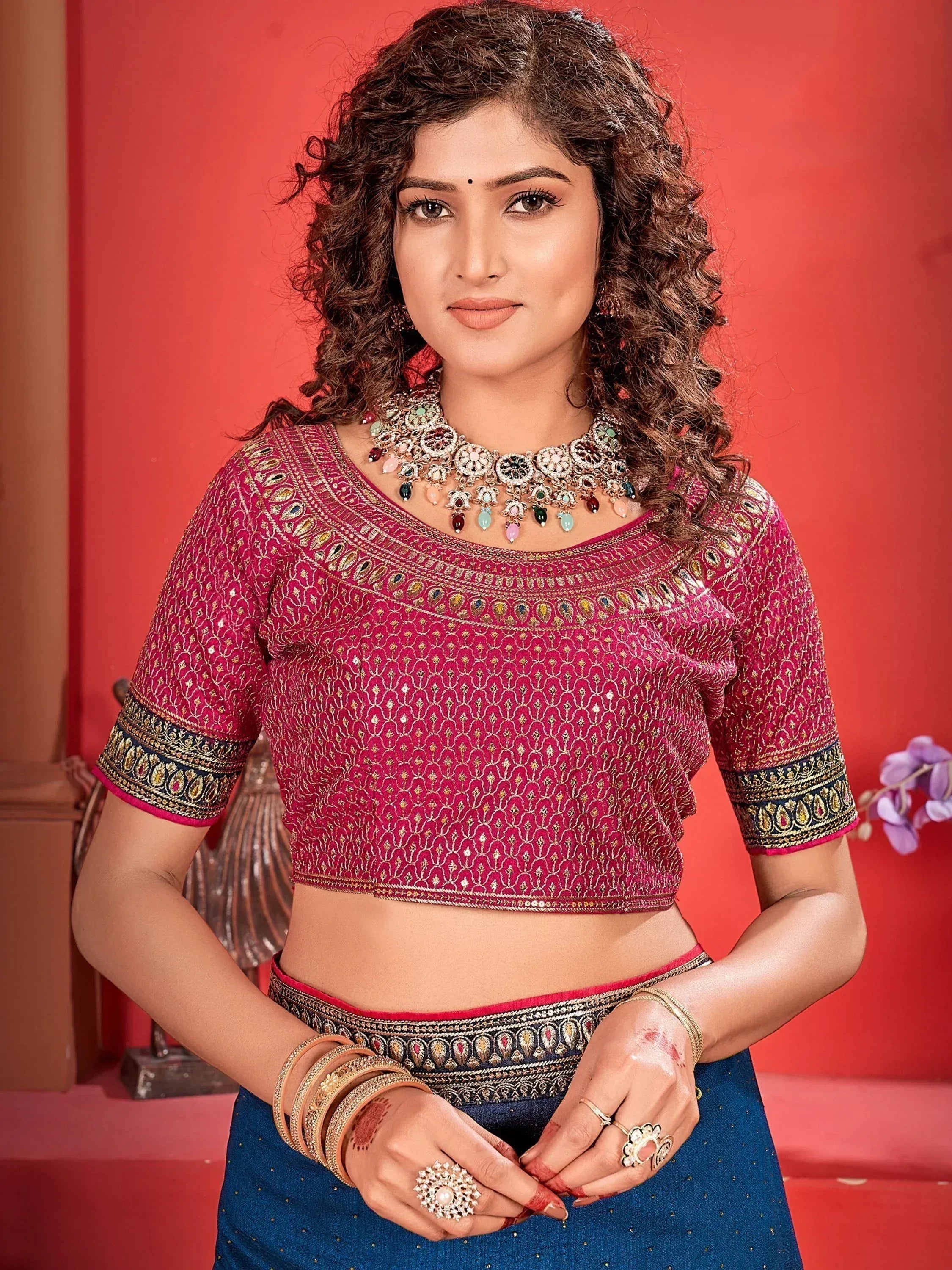 Pink embroidered lehenga choli blouse with gold detailing, paired with blue skirt and traditional jewelry