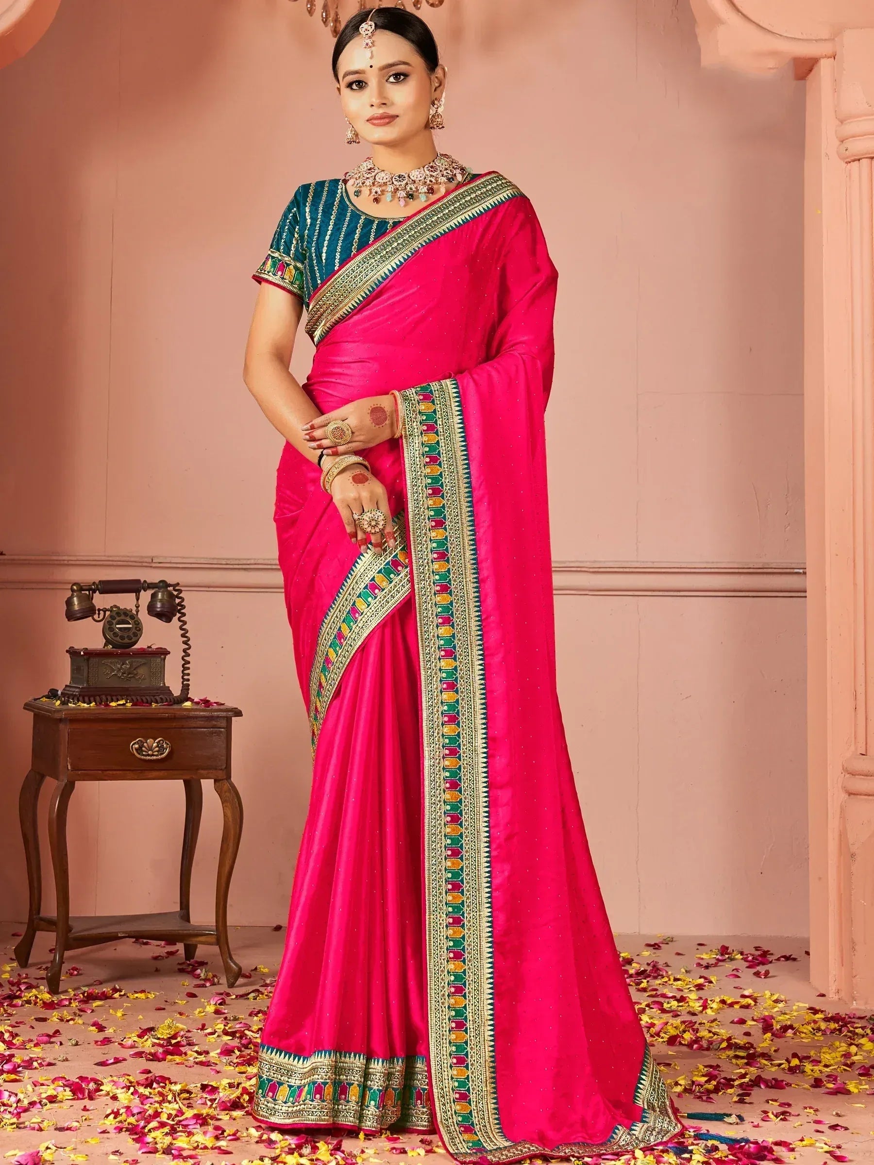 Vibrant pink ethnic saree with colorful border, paired with teal blouse, perfect for Indian celebrations.