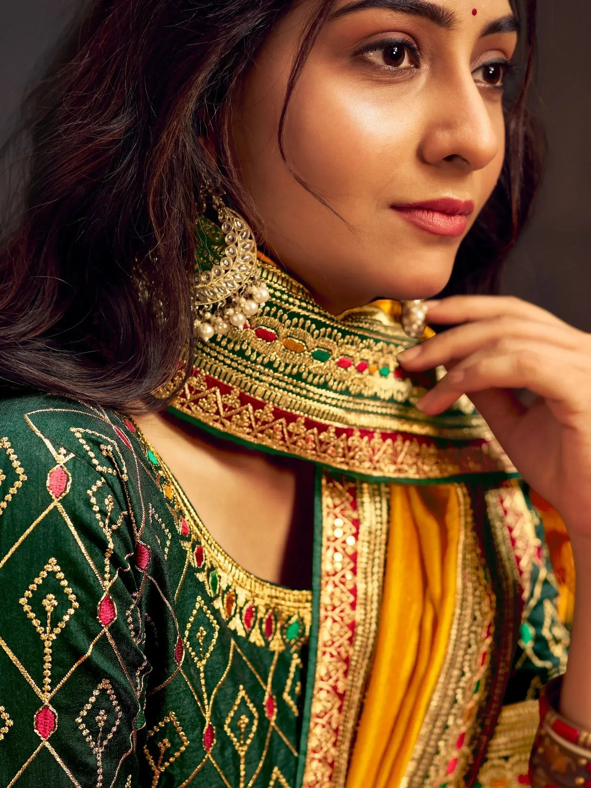 Woman in green embroidered ethnic wear with gold detailing and traditional jewelry