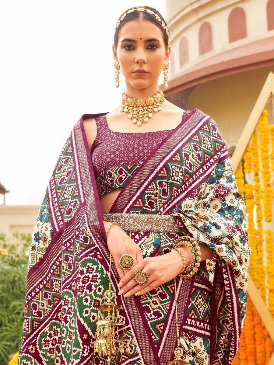 Woman in vibrant purple and green ethnic saree with intricate patterns, traditional jewelry, and temple backdrop
