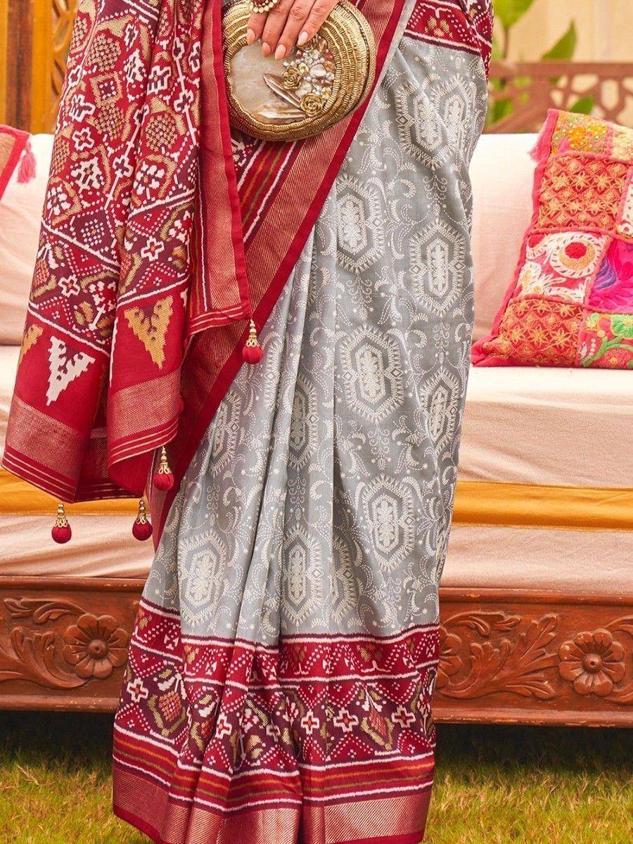 Grey and red ethnic saree with intricate patterns, paired with a decorative clutch, perfect for Indian occasions.