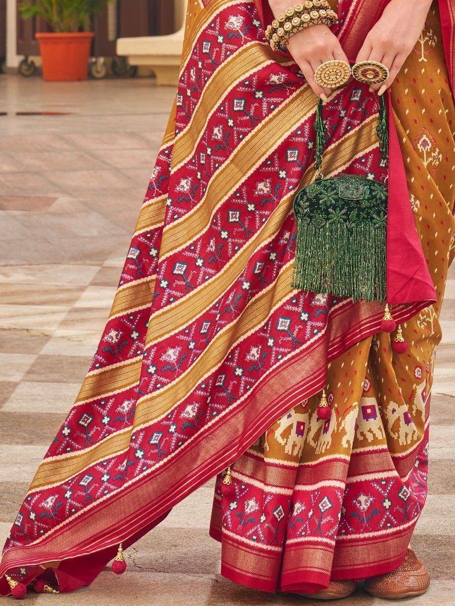 Red and gold ethnic saree with elephant print, tassels, and green embroidered clutch, styled for Indian occasions