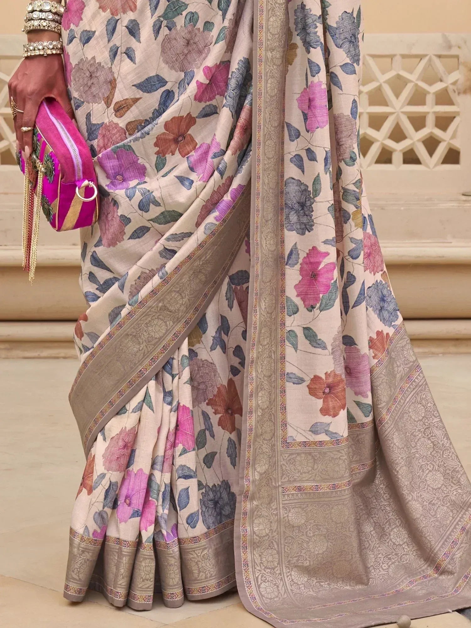 Floral print saree with intricate border, paired with pink clutch and ethnic jewelry for traditional Indian wear