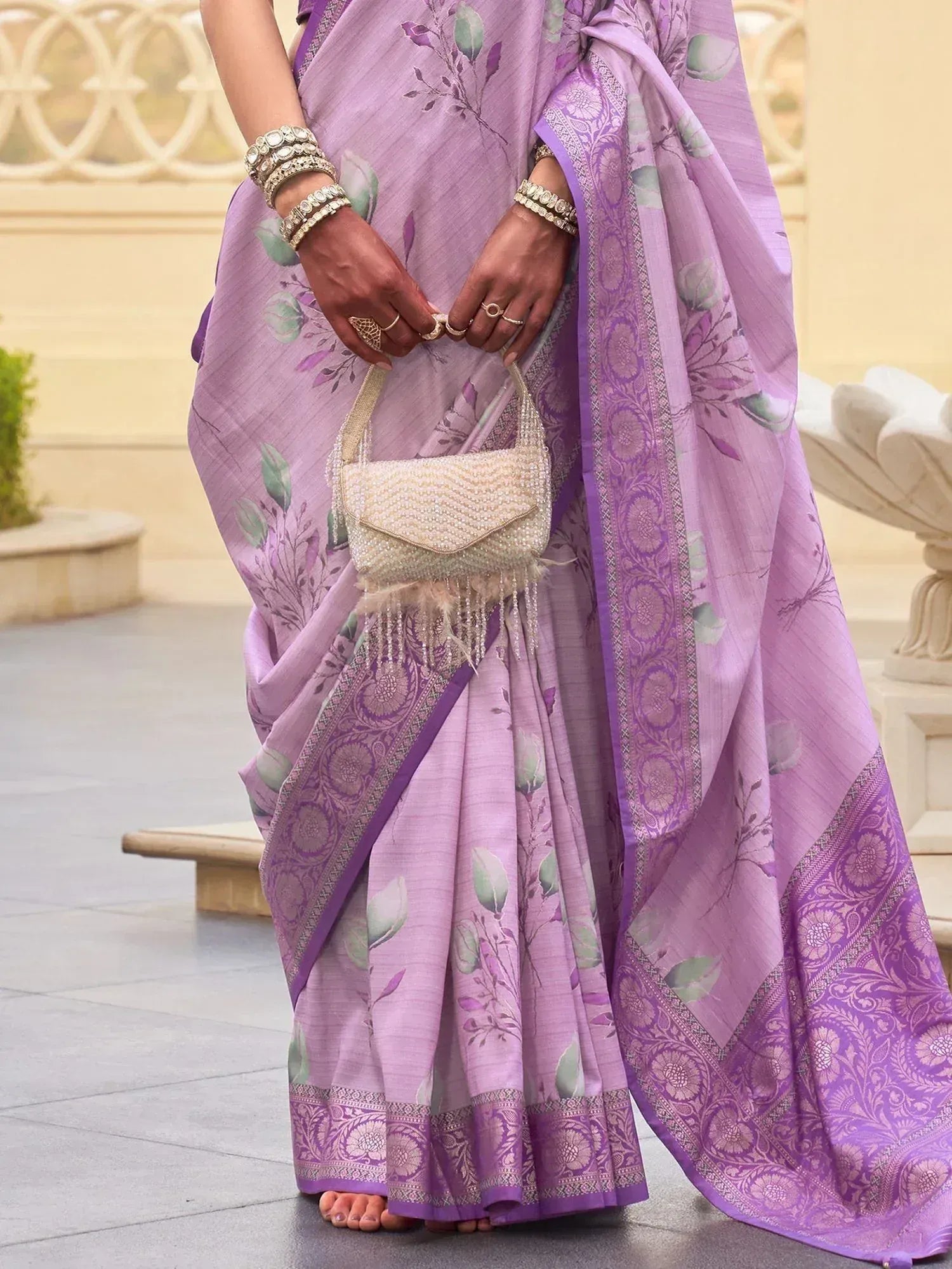 Purple floral printed saree with embroidered border, paired with pearl handbag and traditional jewelry