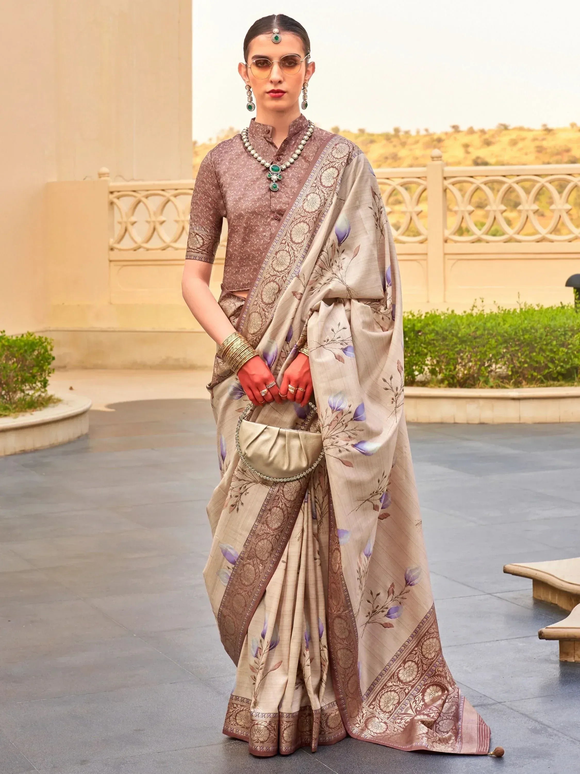 Elegant beige saree with purple floral print and gold border, paired with matching blouse and traditional jewelry