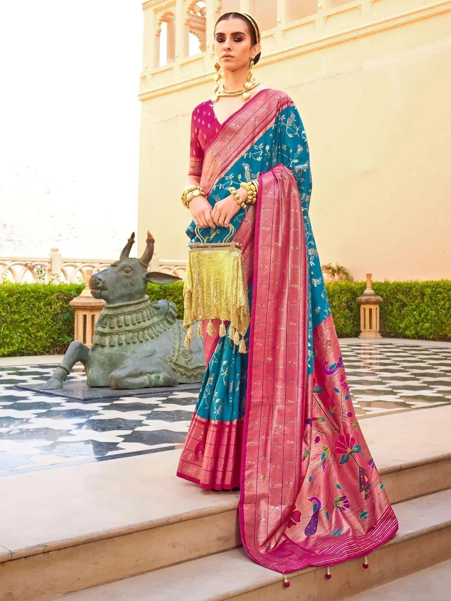 Teal and pink embroidered saree with peacock motifs, styled with gold jewelry and clutch, perfect for Indian ethnic occasions.