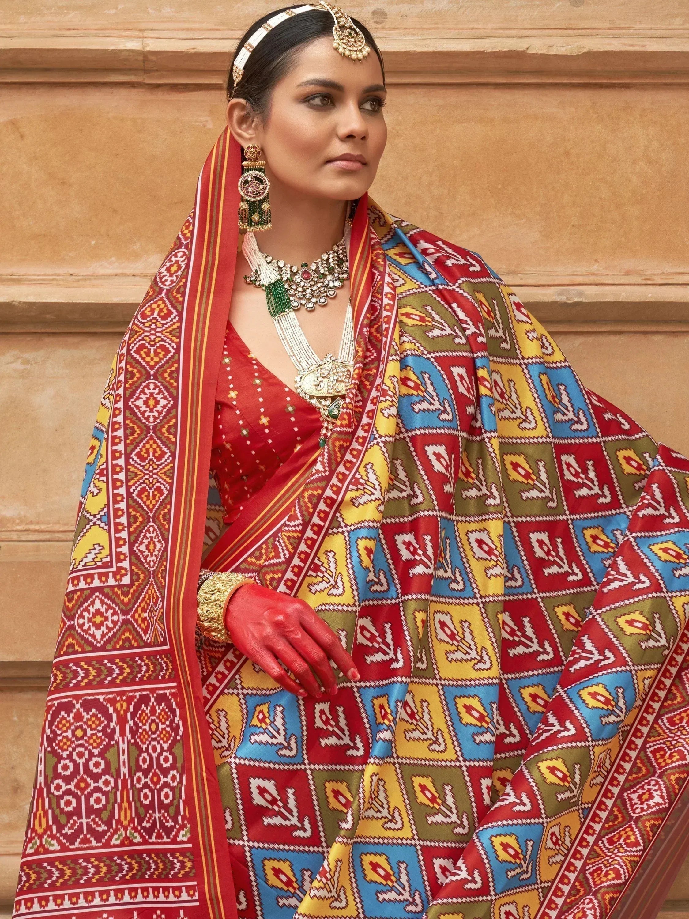 Woman in vibrant Indian saree with geometric print, traditional jewelry, and red blouse, styled for ethnic occasions.