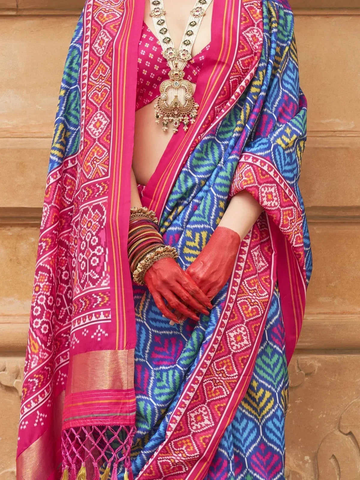 Vibrant pink and blue printed saree with ethnic patterns, paired with gold jewelry and red henna hands