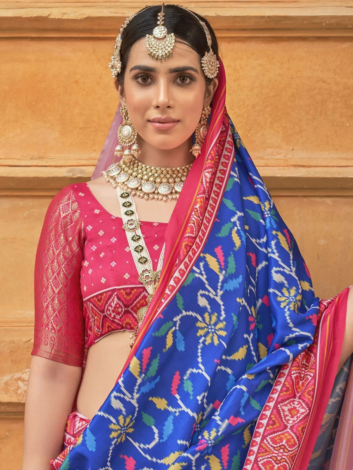 Woman in vibrant blue and pink ikat saree with gold jewelry, traditional Indian ethnic wear