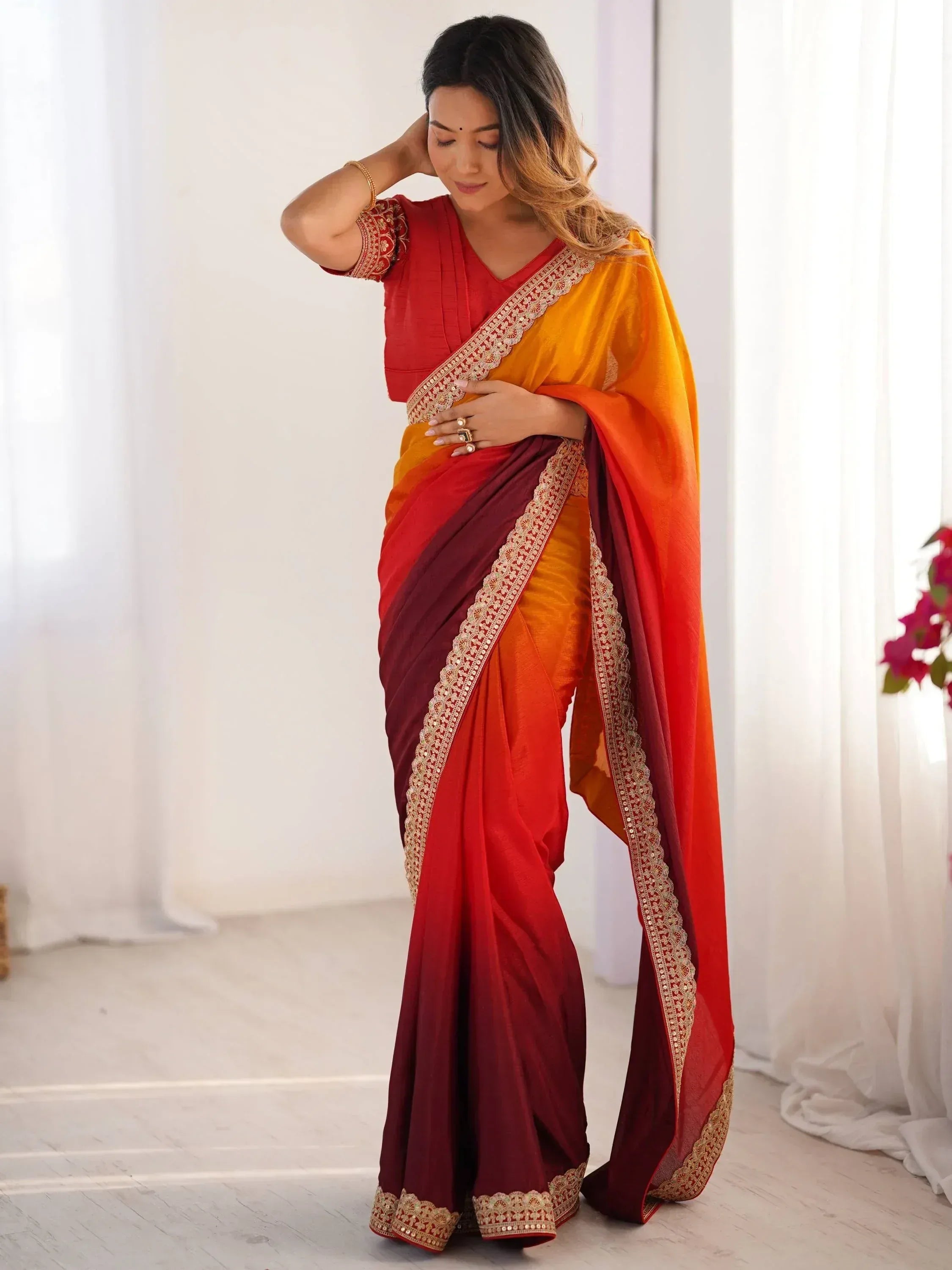 Woman in vibrant red and orange ombre saree with gold embroidery, styled for Indian ethnic wear
