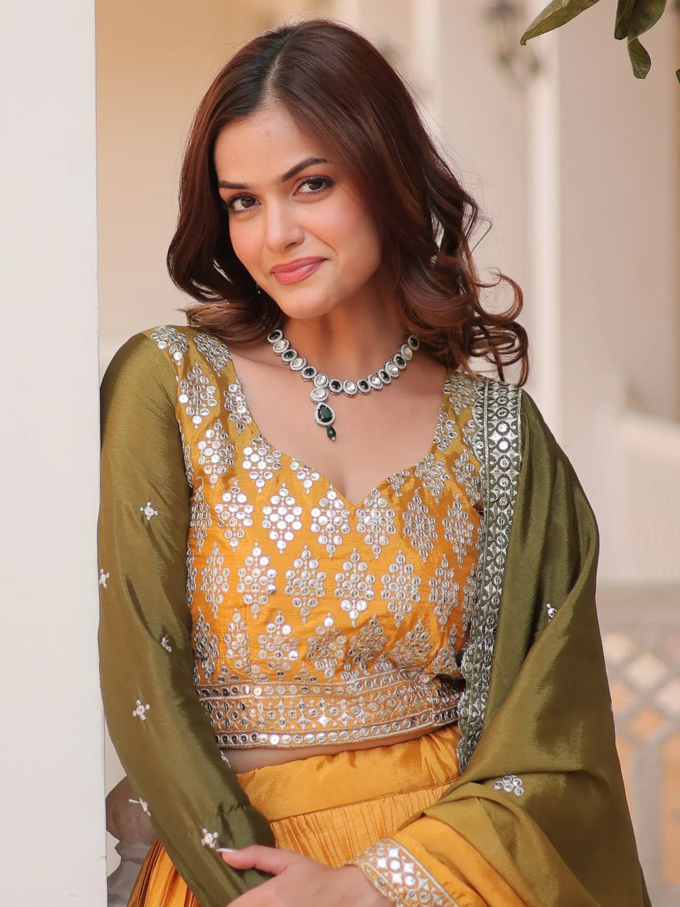 Woman in mustard yellow ethnic lehenga choli with silver mirror work and olive dupatta, styled for festive occasions.